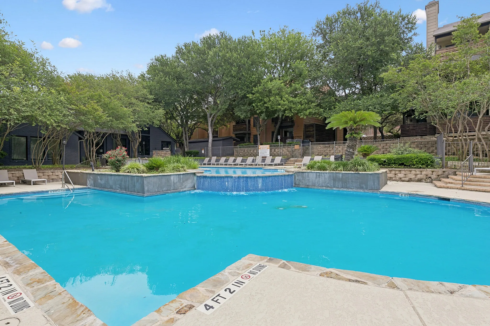 Inviting outdoor pool area with cascading waterfall and lush greenery, perfect for relaxation and leisure.