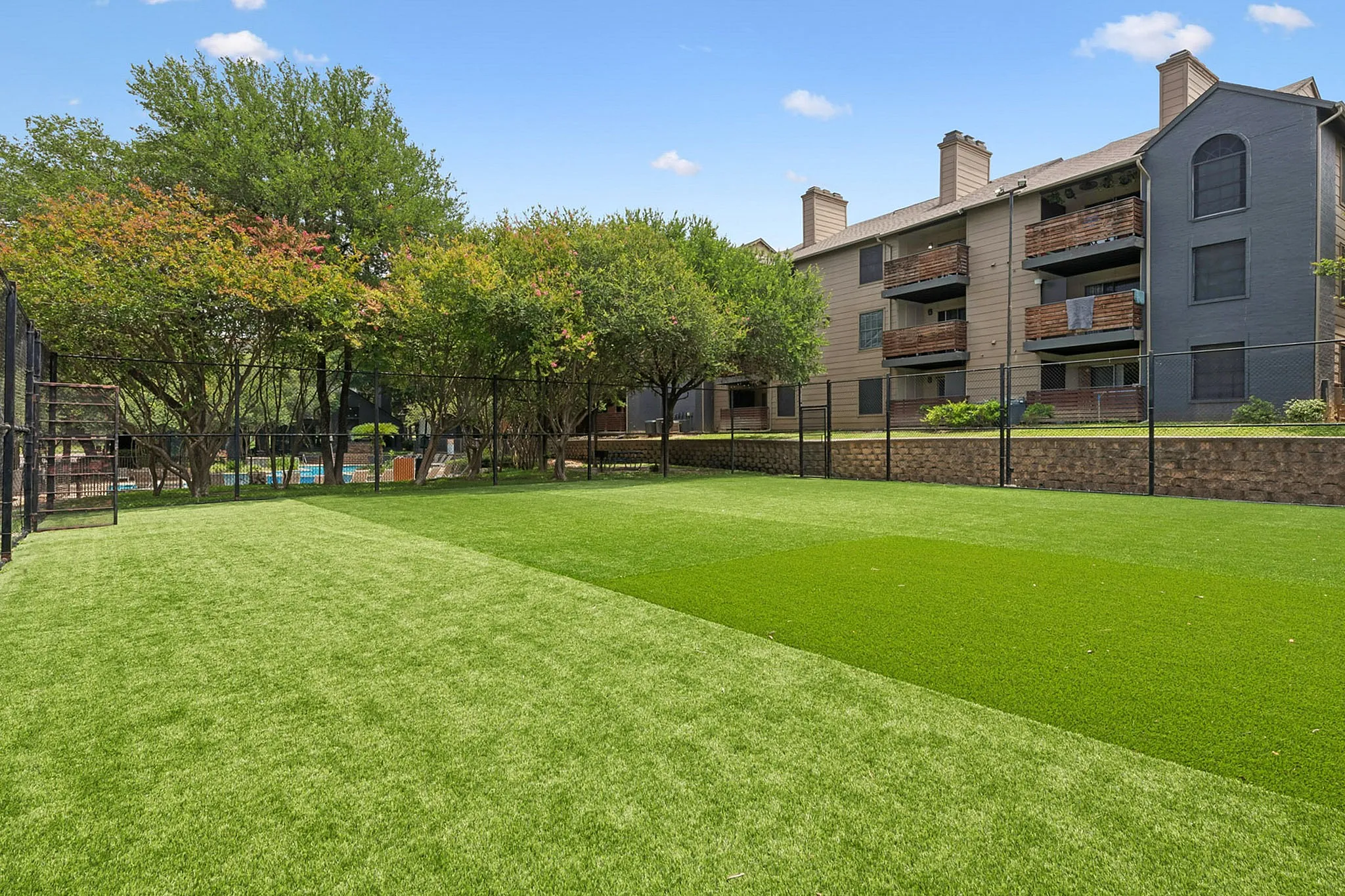 Inviting apartment complex with lush green lawns, mature trees, and spacious balconies offering serene outdoor living.