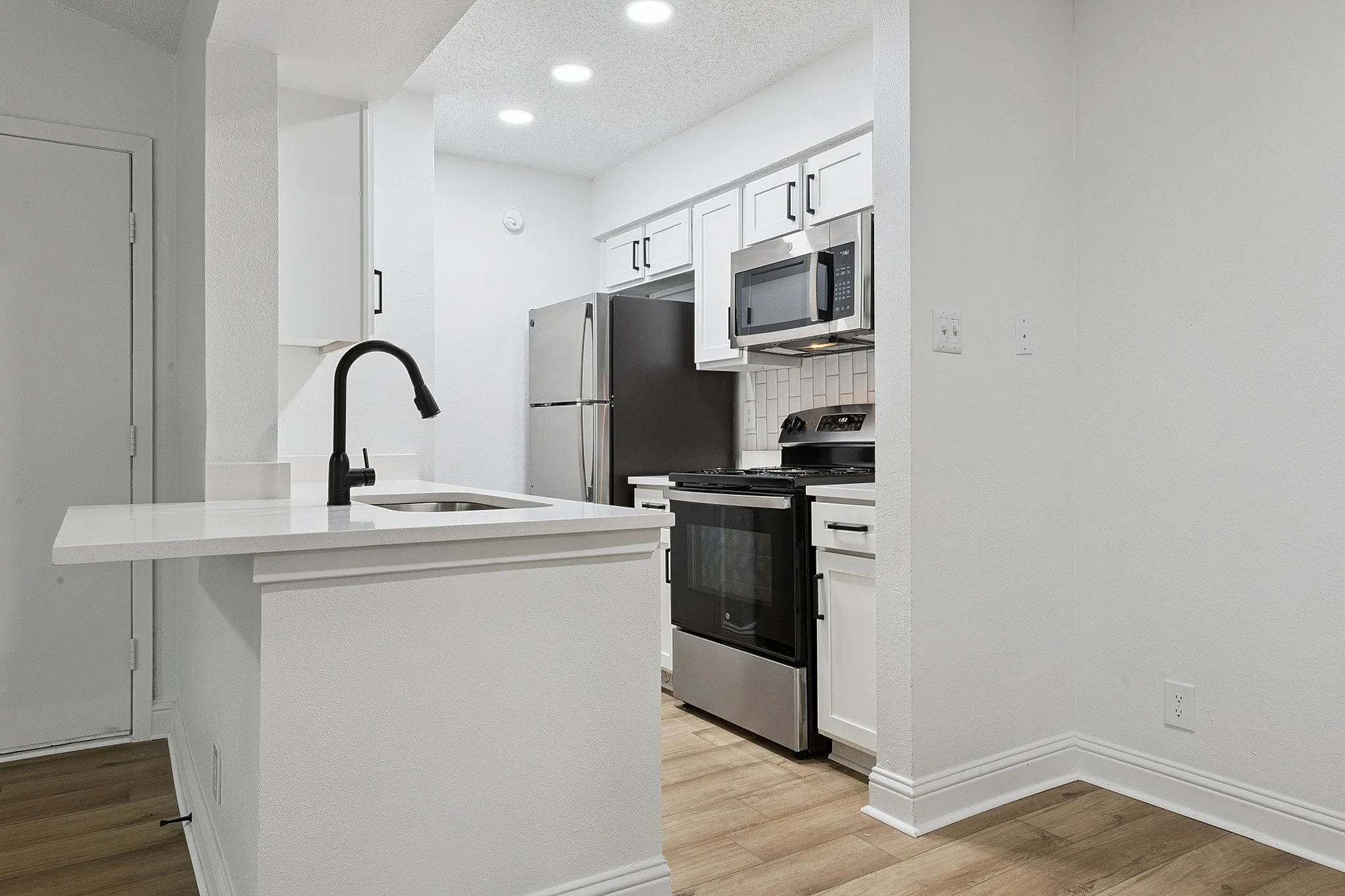 Modern kitchen with sleek stainless steel appliances, elegant white cabinetry, and a chic black faucet over a quartz countertop.