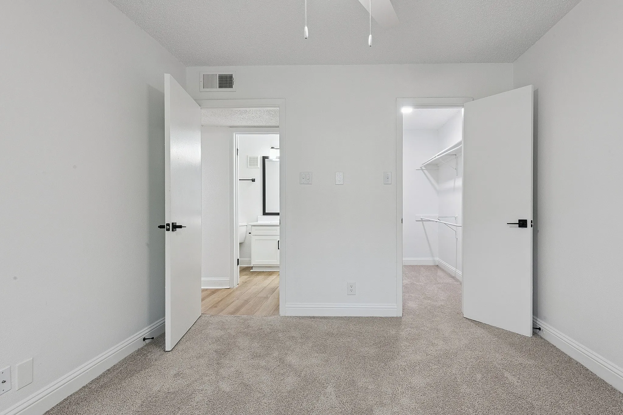 Bright bedroom with plush carpet, leading to a spacious walk-in closet and modern bathroom, perfect for comfortable living.