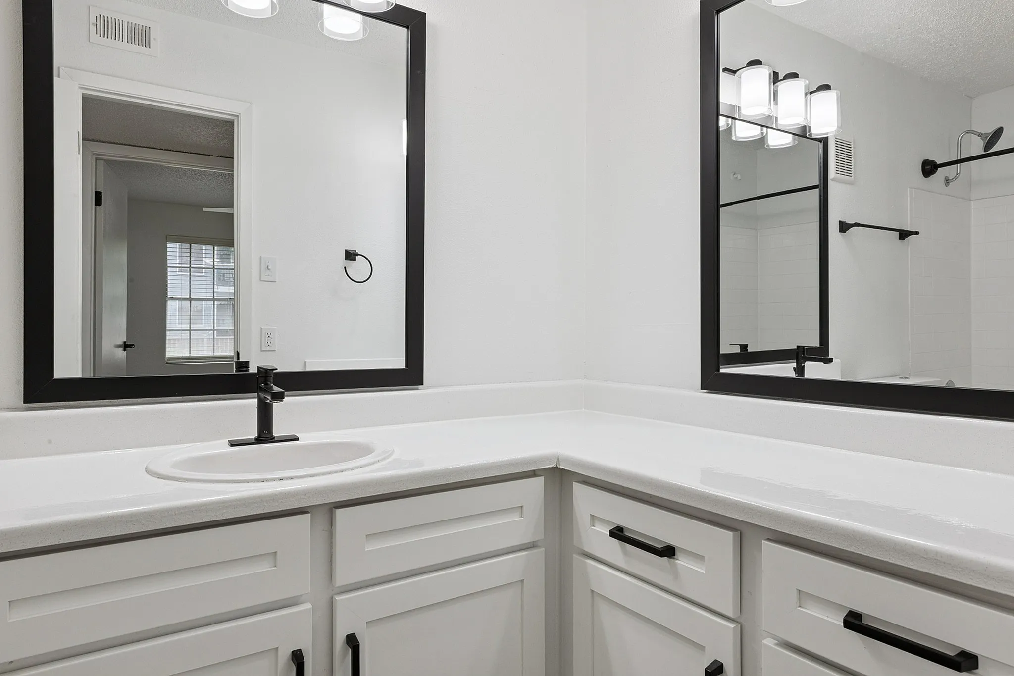 Modern bathroom with sleek black-framed mirrors, bright lighting, and crisp white cabinetry.