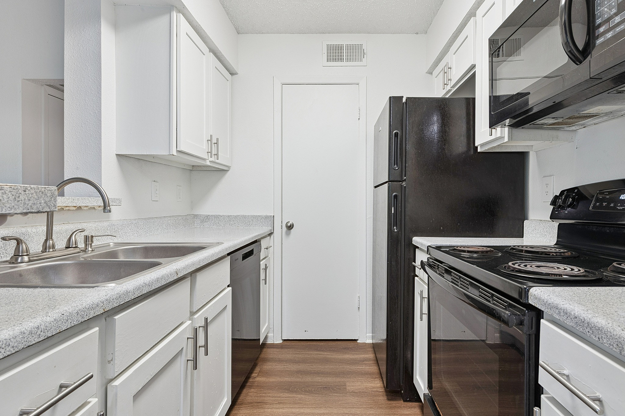 Modern kitchen with sleek white cabinets, black appliances, dual sink, and elegant granite countertops.