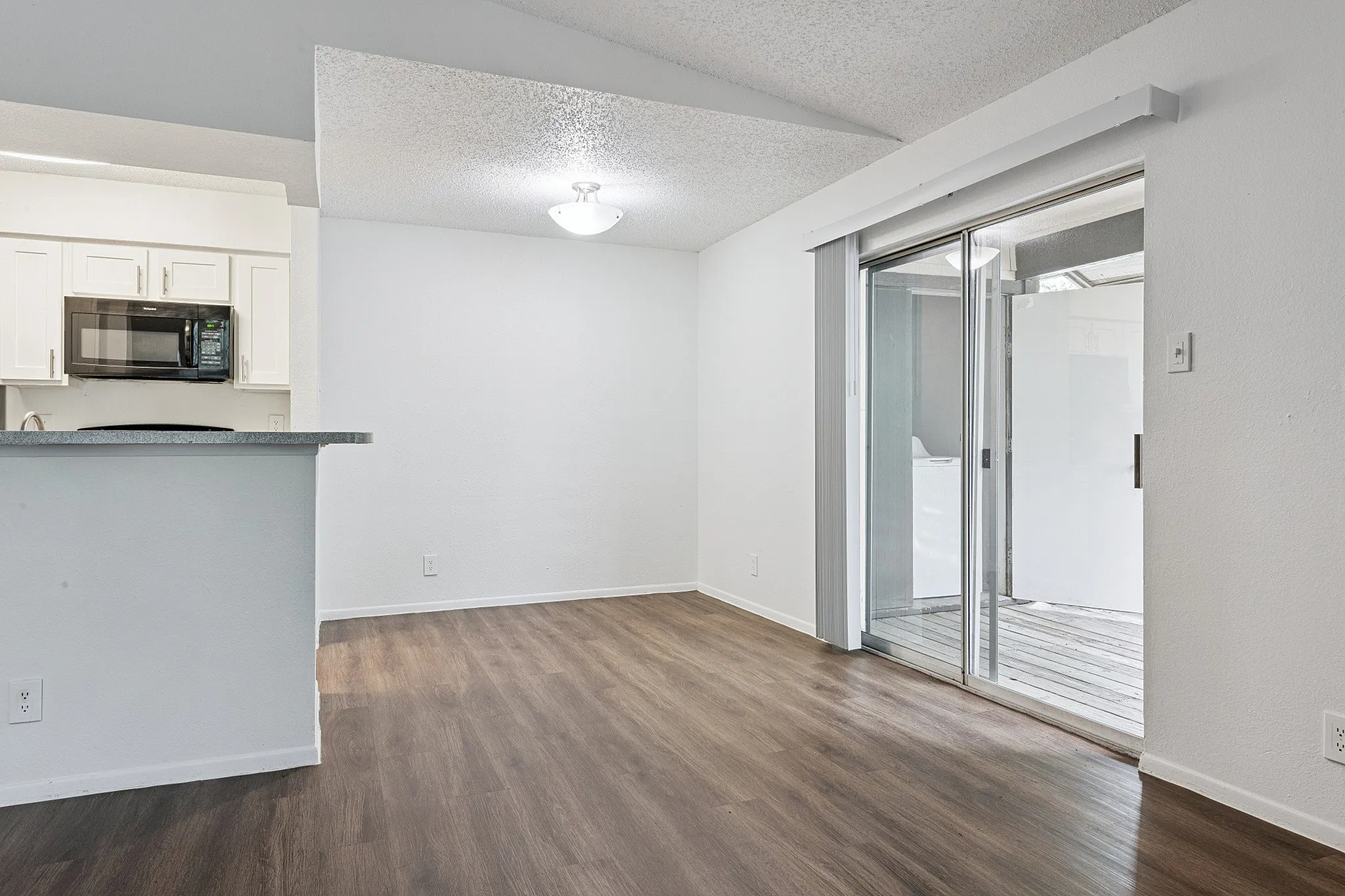 Bright and modern apartment featuring sleek hardwood flooring, a spacious open-plan kitchen with a stylish countertop, and access to a private balcony through sliding glass doors.