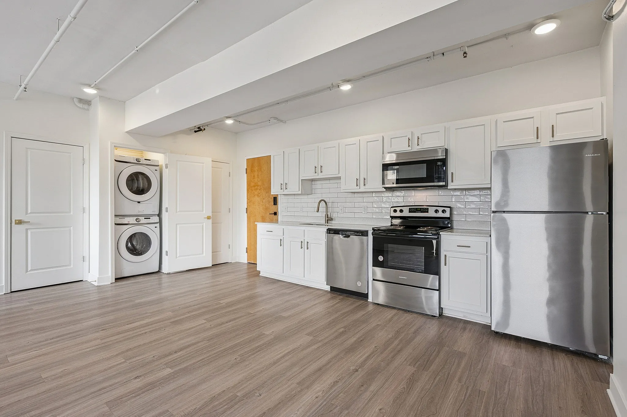 Modern kitchen with sleek stainless steel appliances, stylish white cabinetry, and in-unit laundry for convenience.