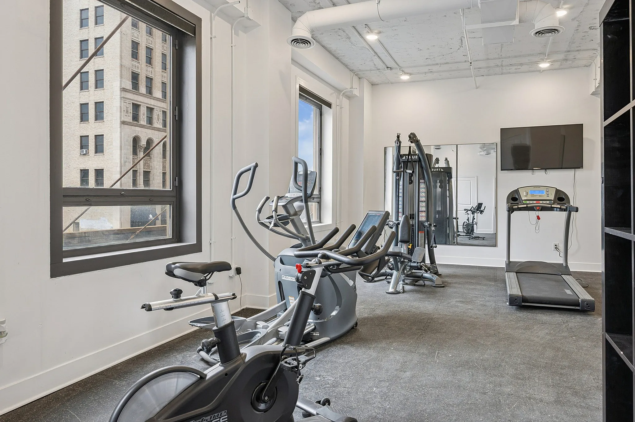 Modern apartment gym with state-of-the-art exercise equipment and large windows offering a city view.