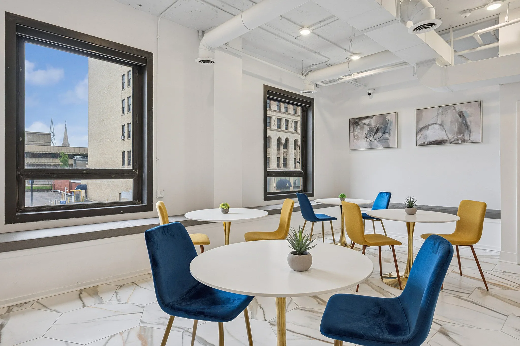 Contemporary dining area with bold blue and yellow chairs, chic round tables, and large windows offering a vibrant city view.