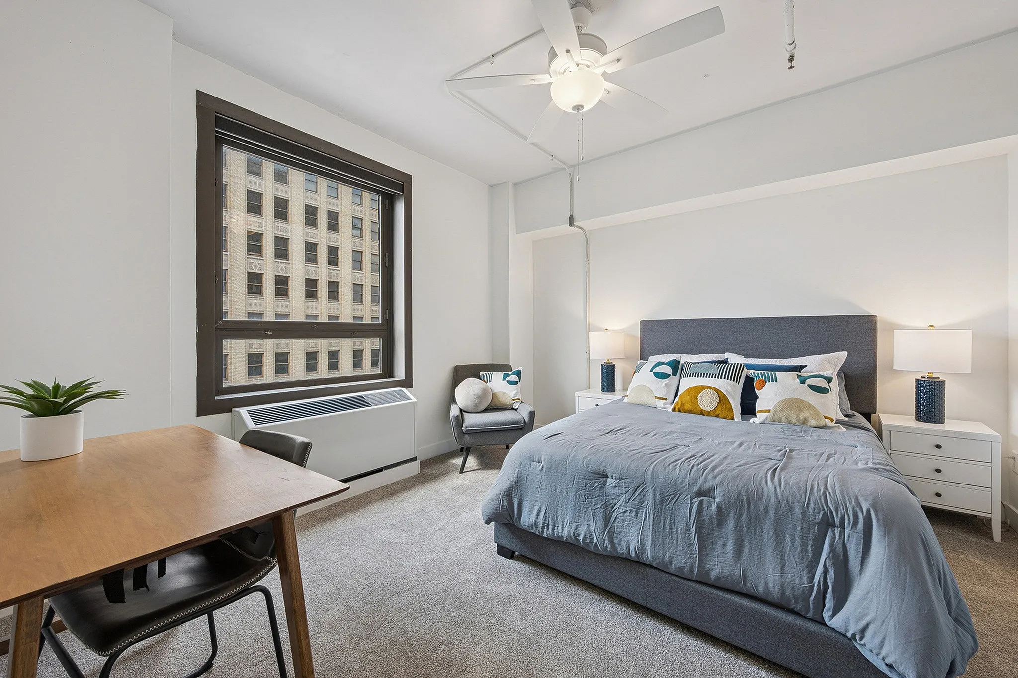 Bright and inviting bedroom with a plush bed, modern furnishings, and large window offering city views.