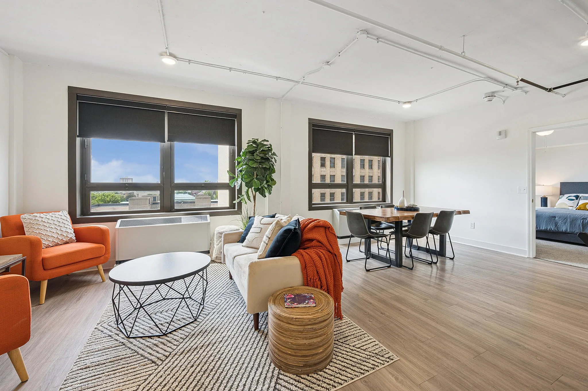 Modern living space with stylish decor, featuring large windows, cozy seating area, and elegant dining space leading to a inviting bedroom.