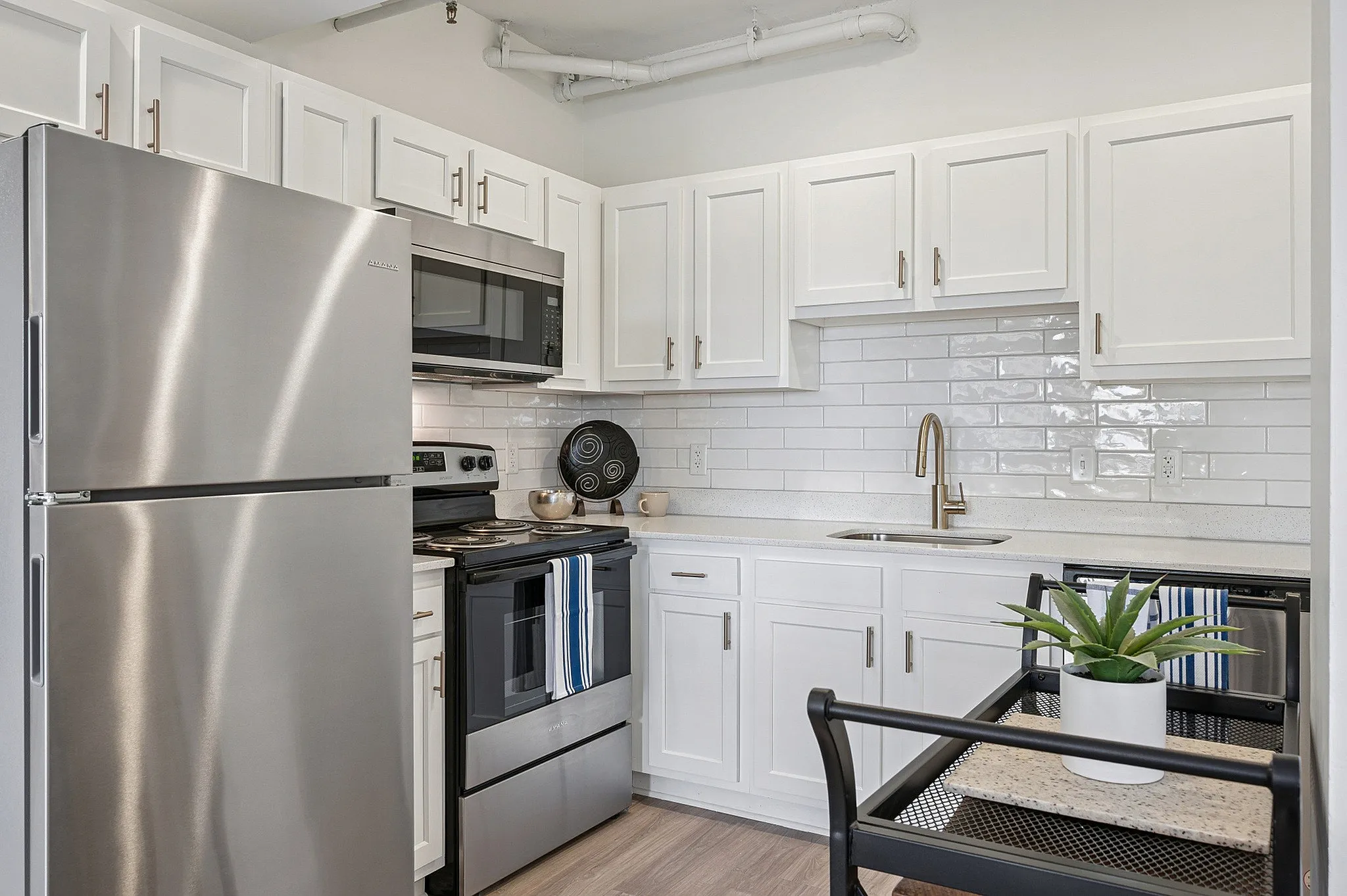 Modern kitchen featuring sleek stainless steel appliances, chic white cabinetry, and elegant subway tile backsplash, complemented by warm hardwood floors.