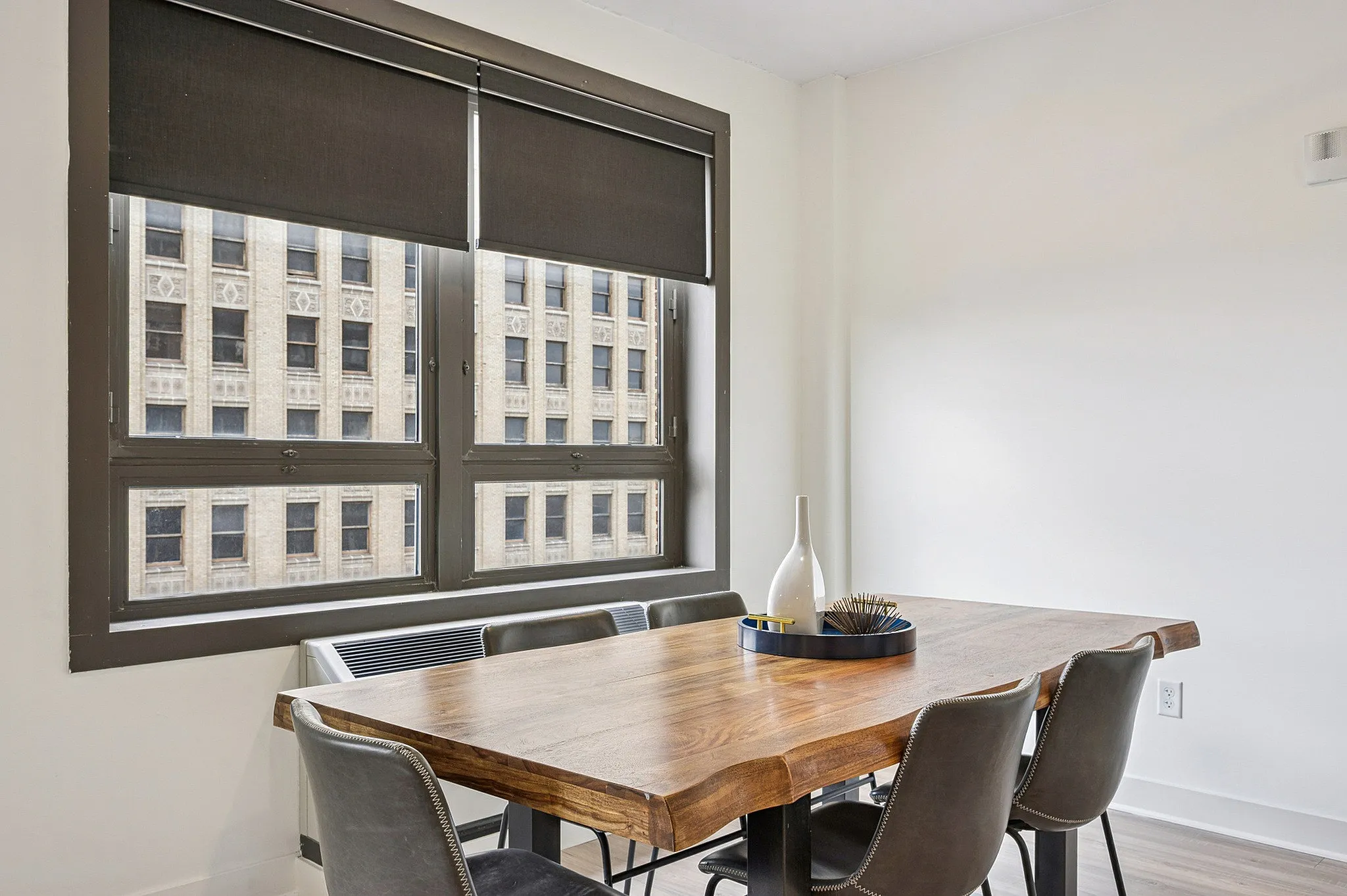 Modern dining area with a sleek wooden table and stylish chairs, featuring large windows overlooking a charming historic building.