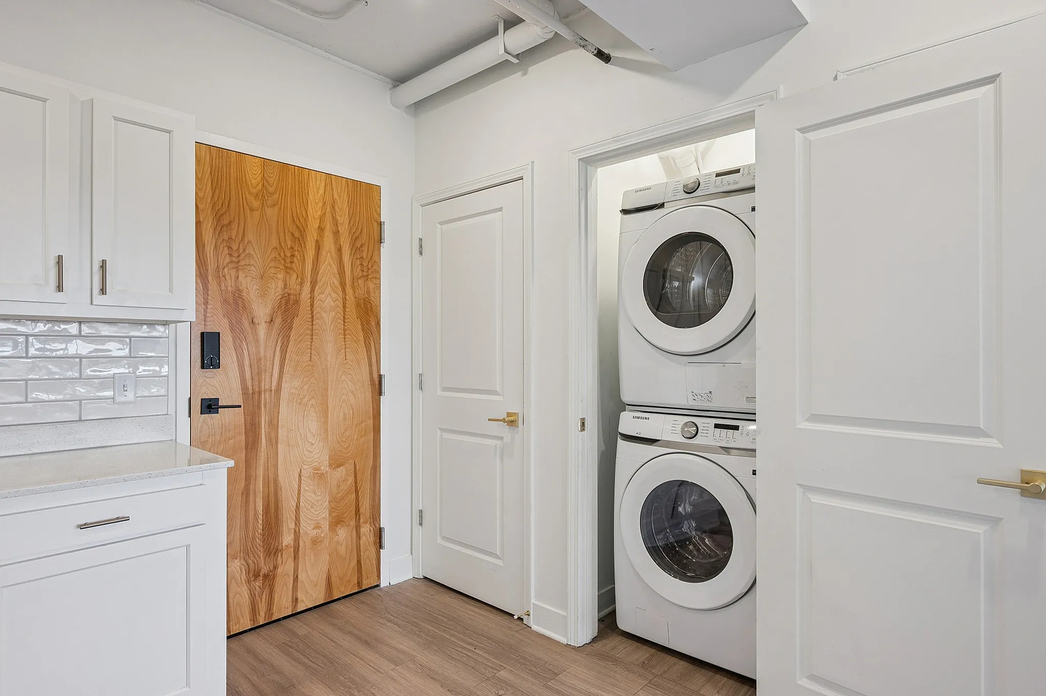 Modern apartment laundry area with sleek stacked washer and dryer, complemented by elegant white cabinetry and warm wooden doors.