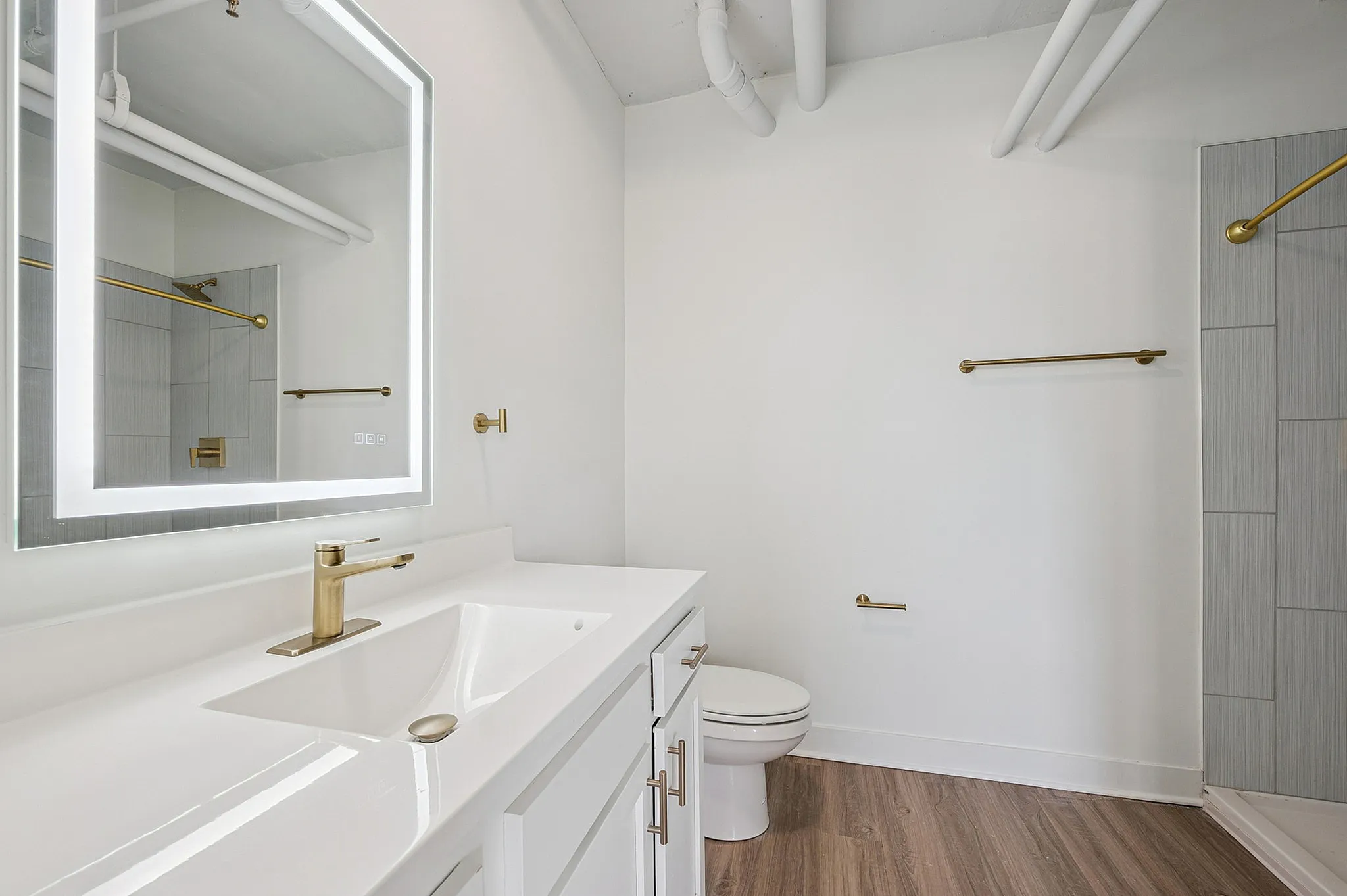 Modern bathroom featuring elegant gold fixtures, a sleek illuminated mirror, and stylish wood flooring.