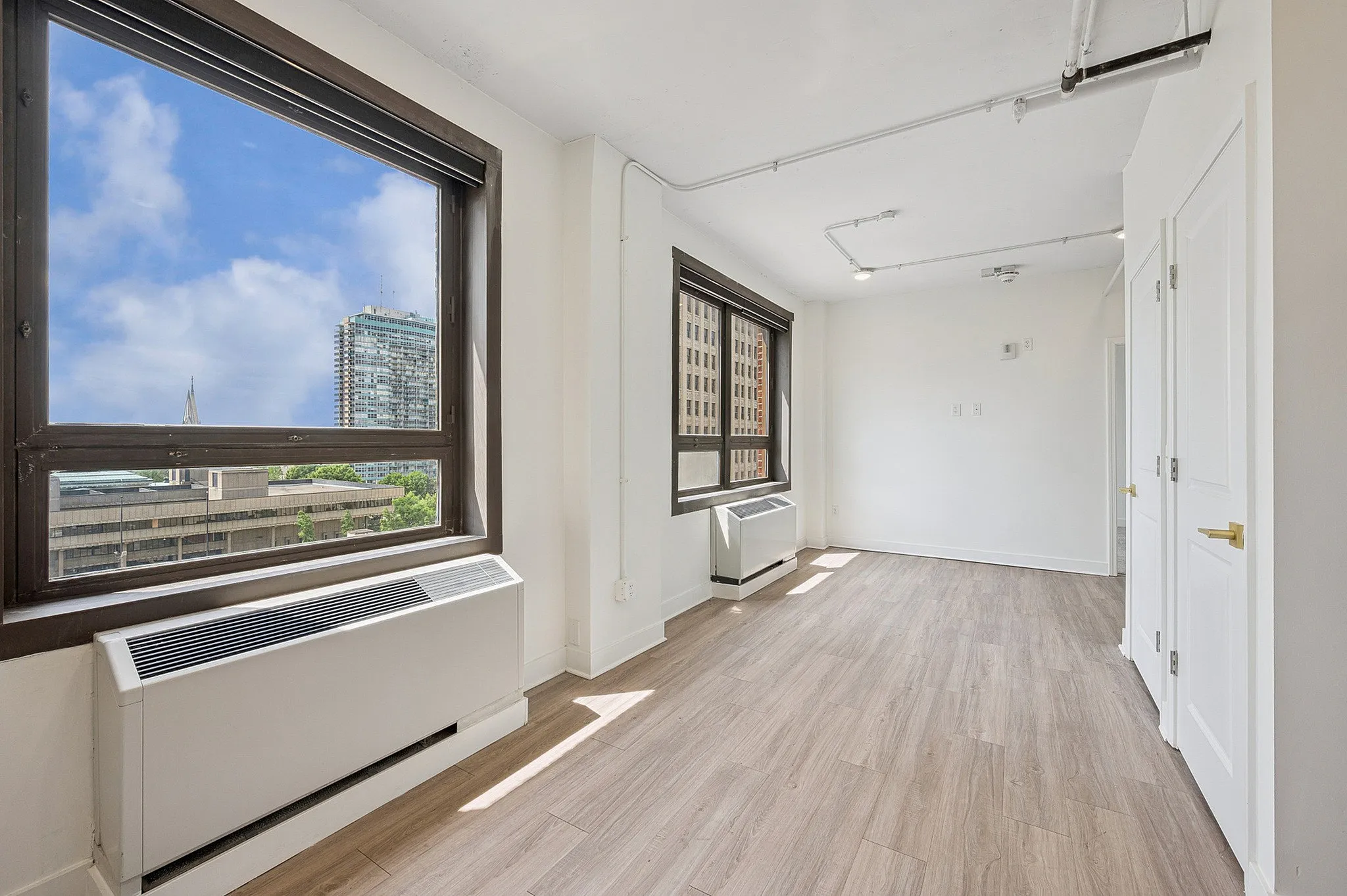 Bright city-view apartment with large windows, sleek wooden flooring, and modern heating ventilation.