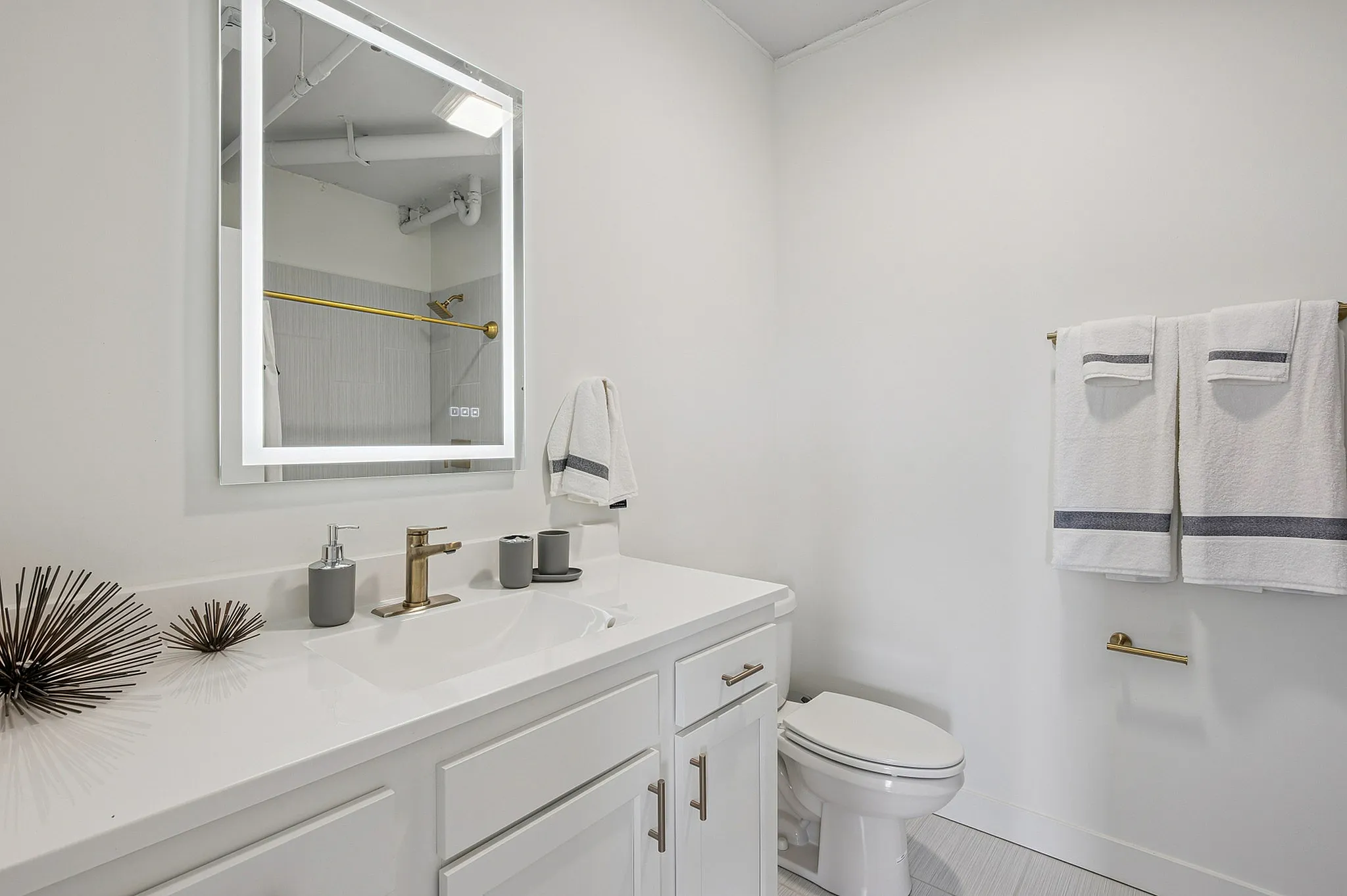 Elegant and modern bathroom featuring a sleek vanity with a gold faucet, stylish illuminated mirror, and plush white towels.