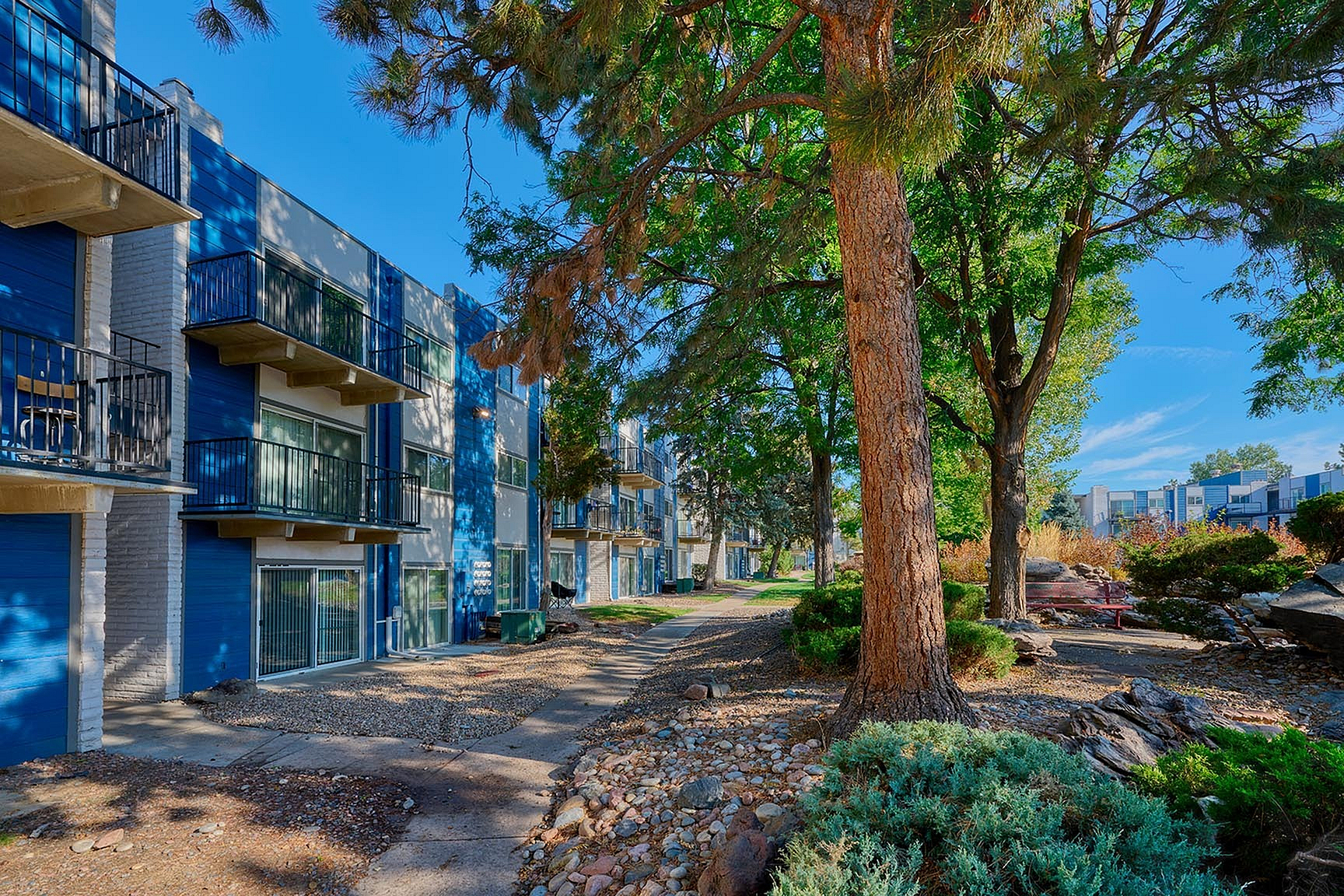 Charming apartment complex with vibrant blue accents, surrounded by lush greenery and serene pathways.
