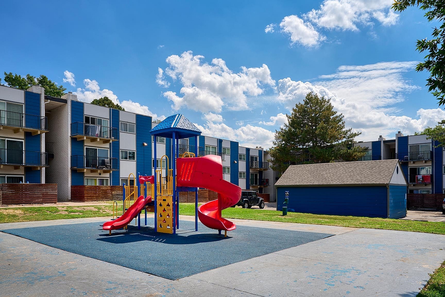 Modern apartment complex with vibrant blue accents, featuring a colorful playground under a clear blue sky, ideal for family living.