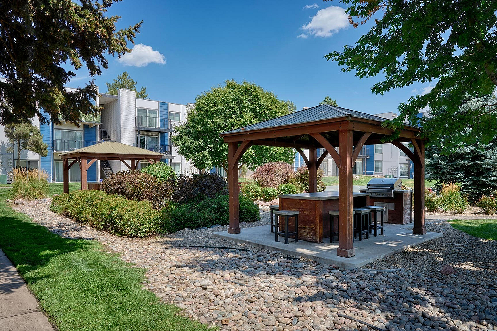 Charming outdoor communal area with a wooden gazebo, barbecue grill, and lush landscaping, perfect for entertaining.