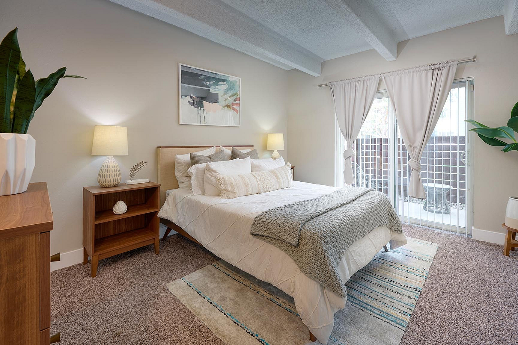 Inviting bedroom with cozy white bedding, modern wooden furniture, elegant decor, and abundant natural light from large windows.