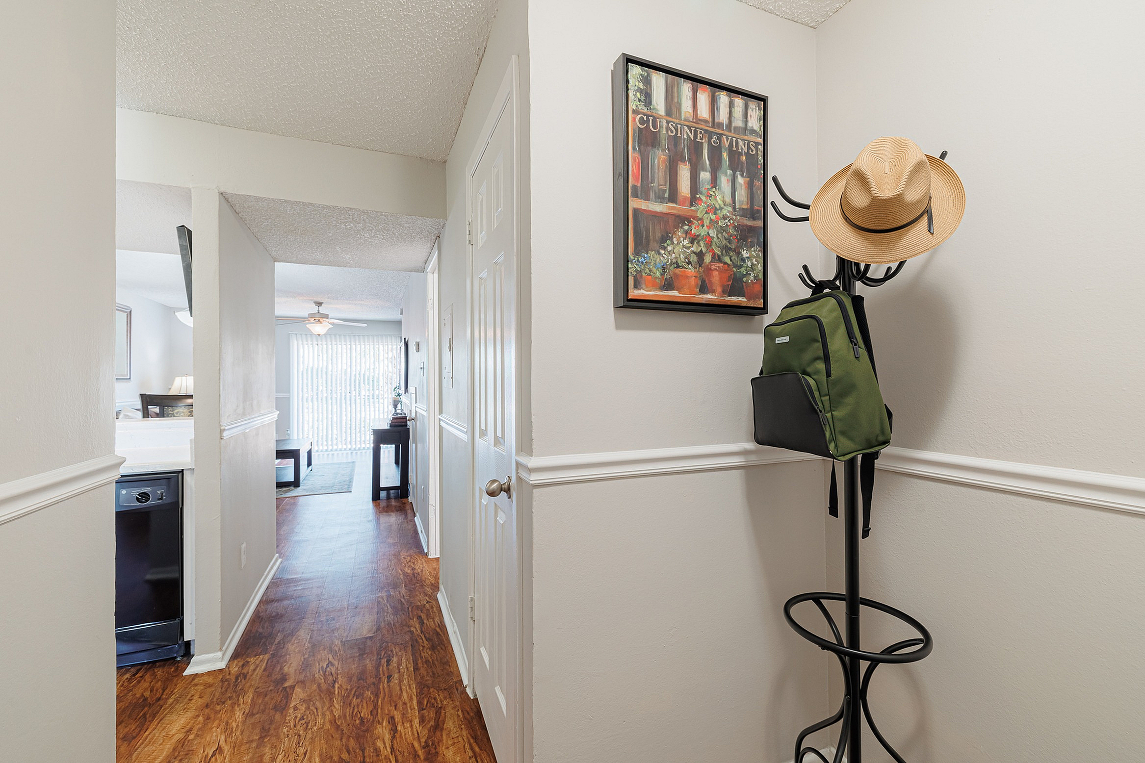 Inviting apartment entrance featuring hardwood floors, decorative wall art, and a stylish coat rack with a hat and backpack.