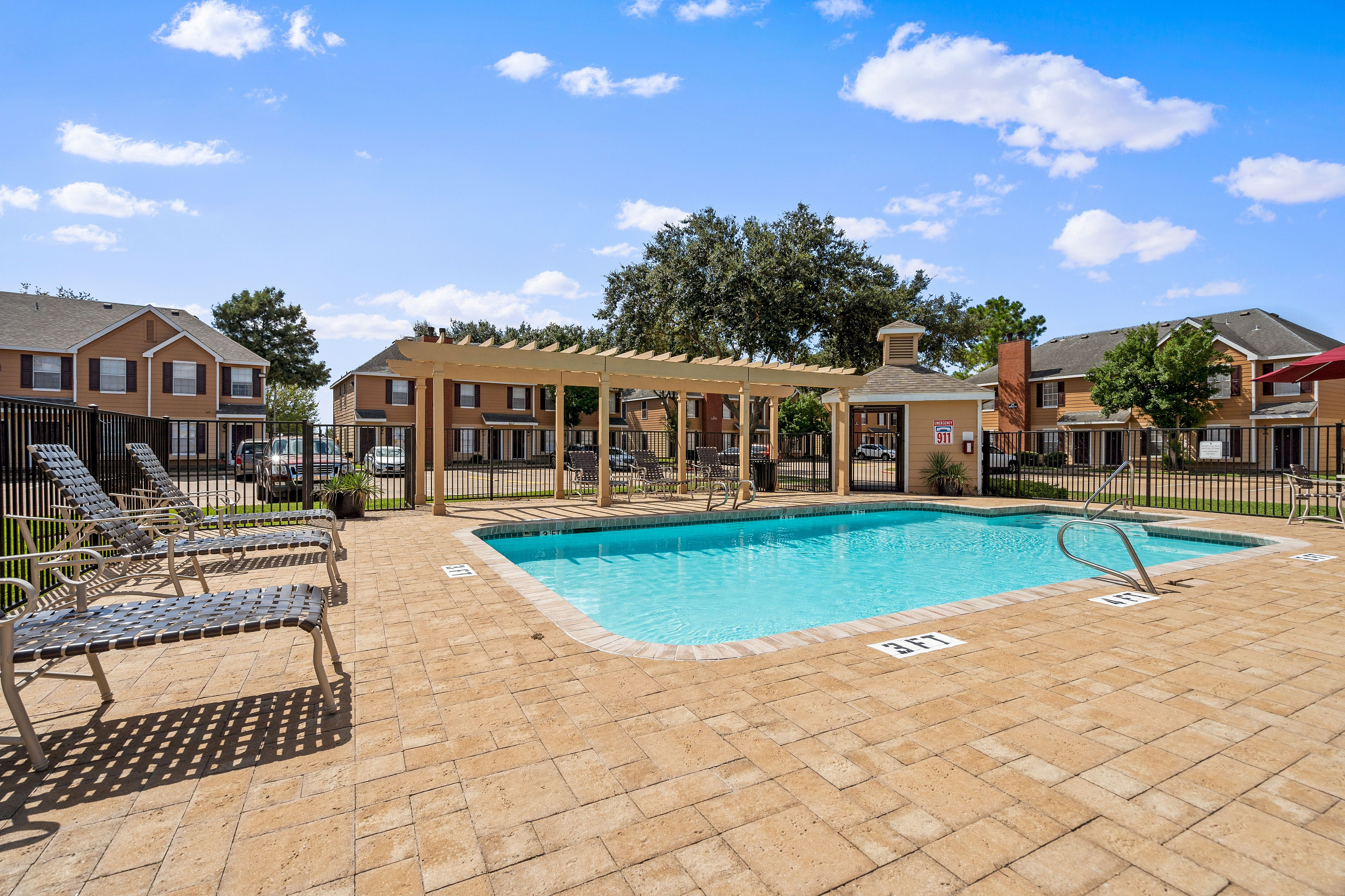 Inviting outdoor pool area with stylish lounge chairs and pergola, nestled within a charming residential community under a bright blue sky.