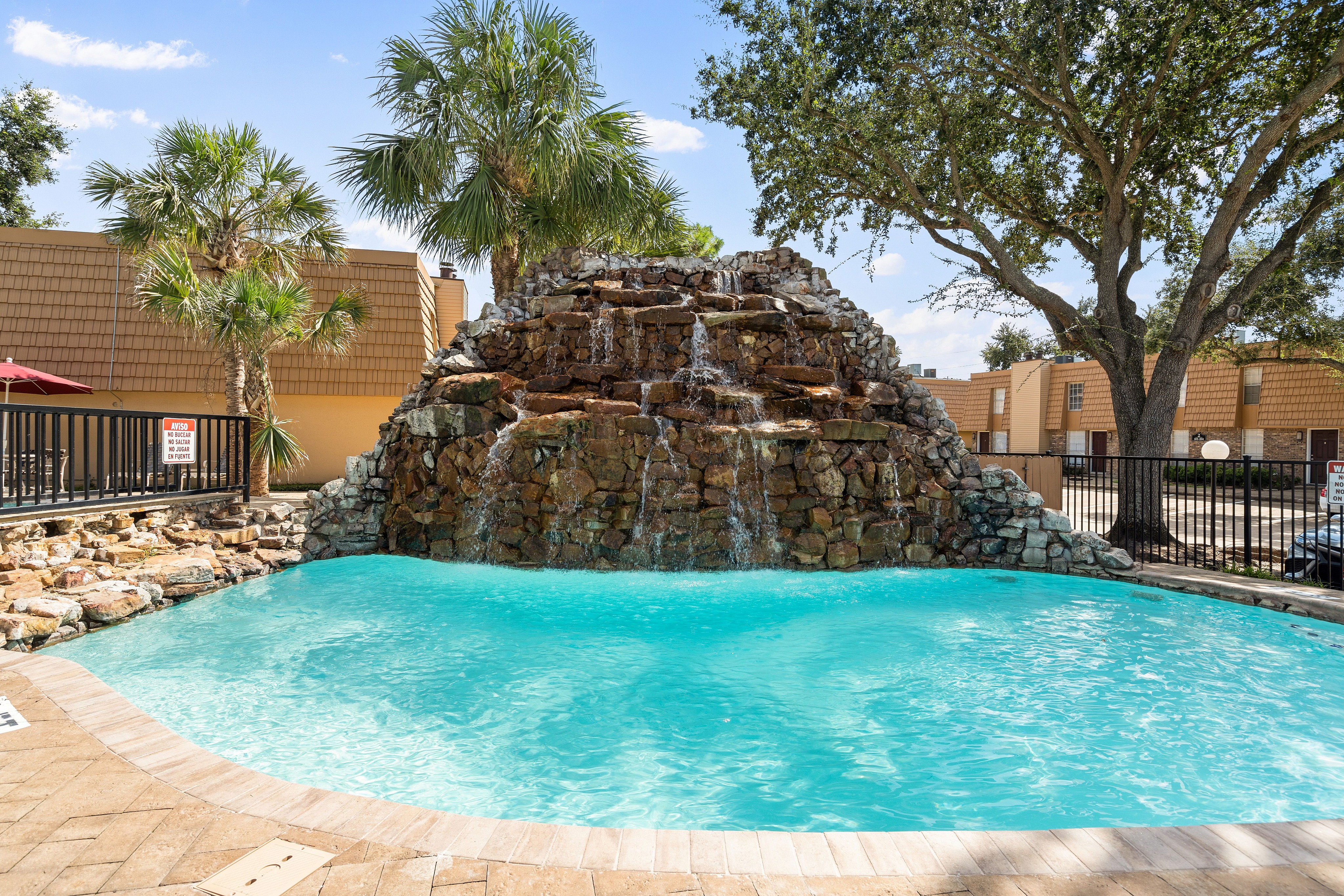 Inviting outdoor pool with cascading waterfall feature and lush palm trees, offering a tropical oasis ambiance at the apartment complex.