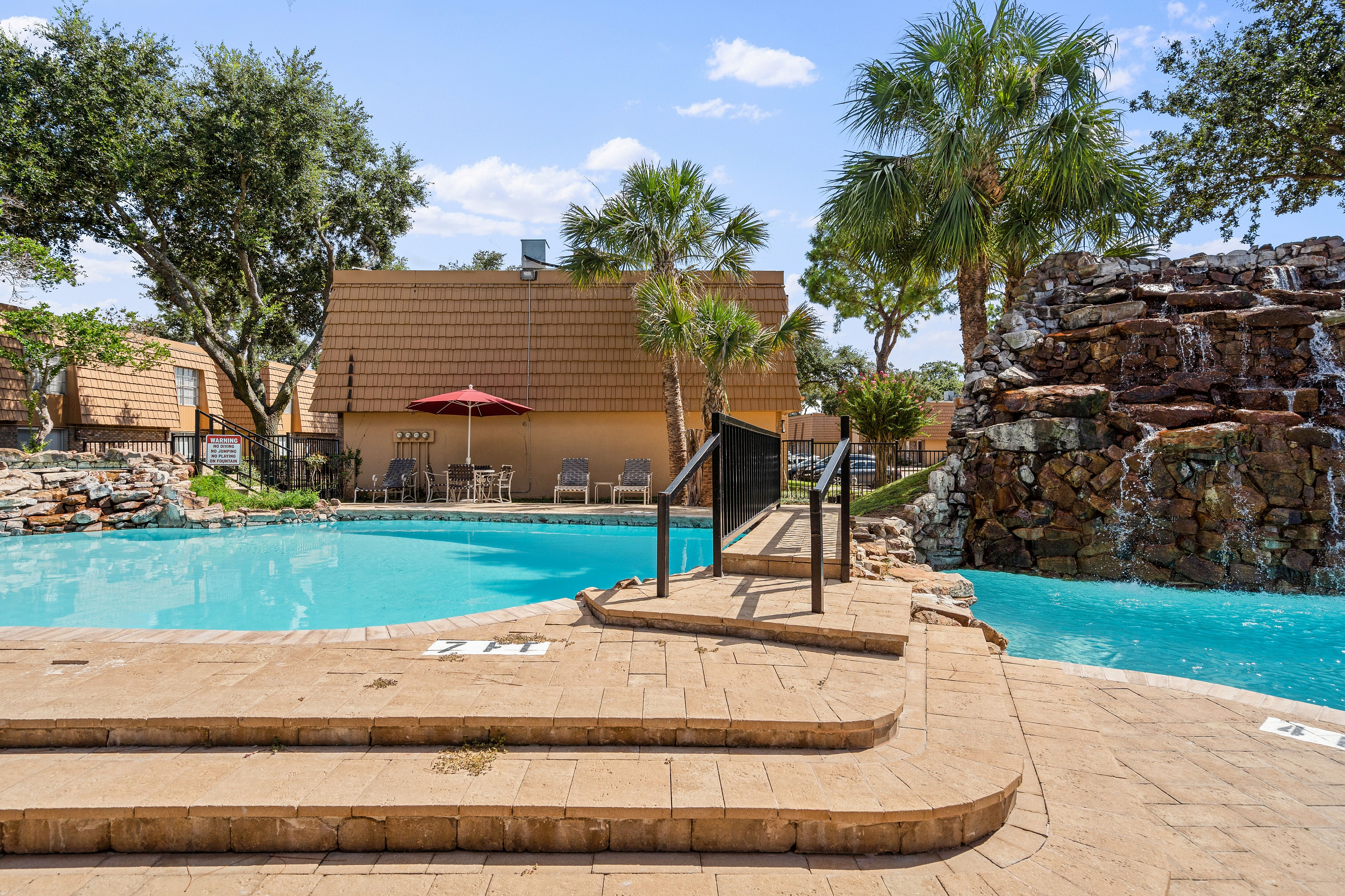 Inviting outdoor pool area with scenic waterfall feature, surrounded by lush palm trees and comfortable lounge seating, perfect for relaxation.