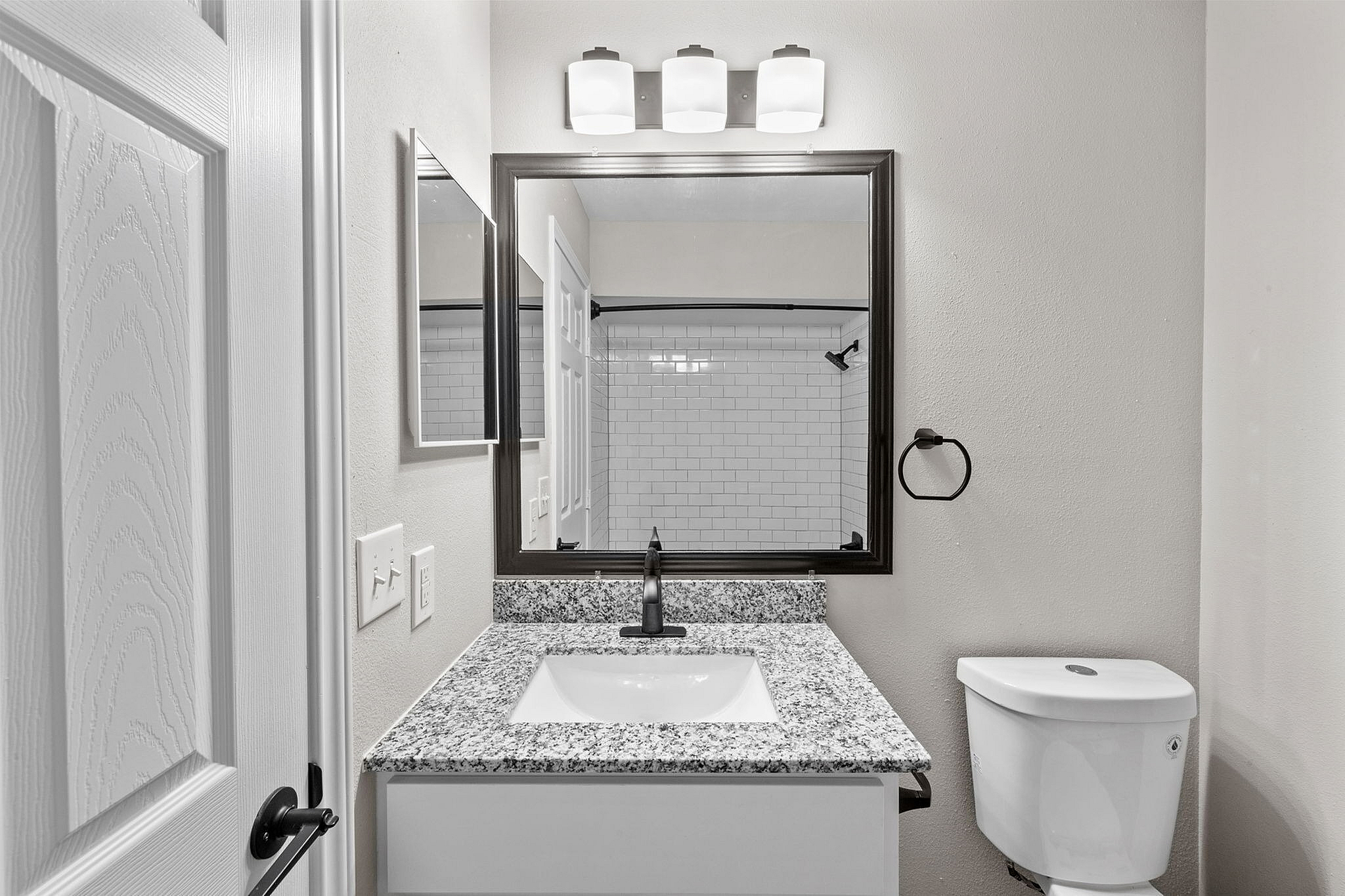 Elegant bathroom with a sleek granite countertop, modern vanity mirror, and chic subway tile shower.
