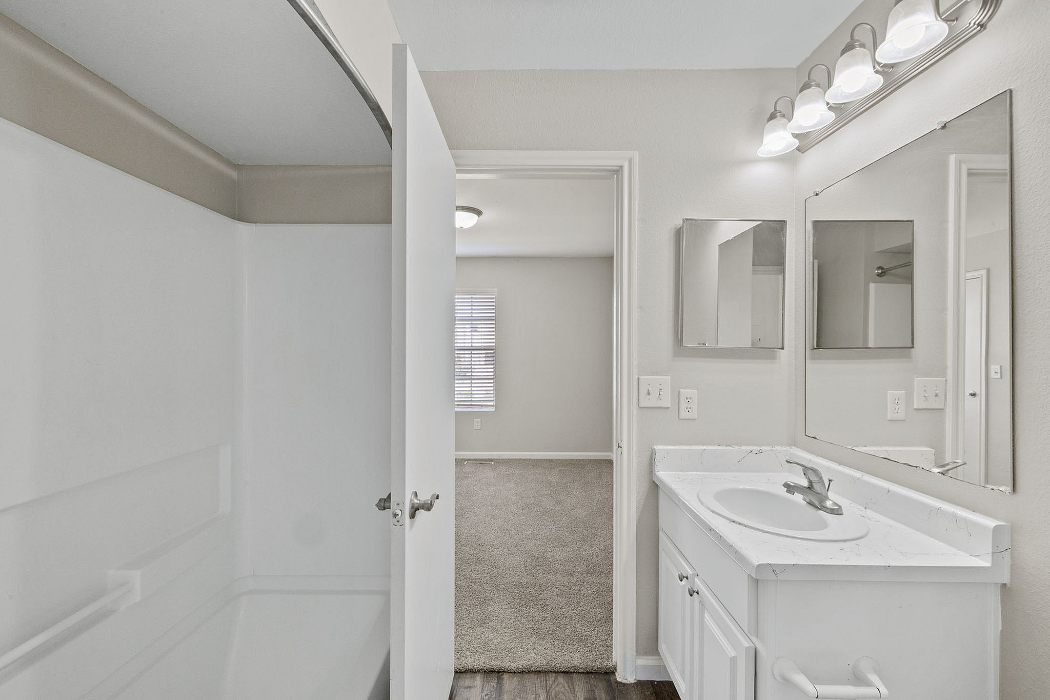 Bright and modern bathroom with elegant fixtures, white marble countertop, and a spacious shower area next to a cozy carpeted bedroom.