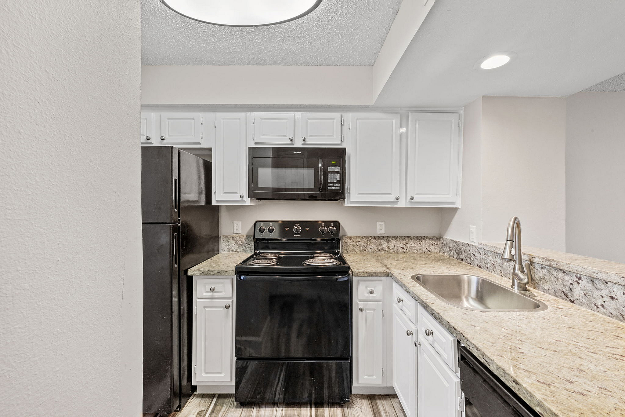 Modern kitchen with sleek granite countertops, stainless steel sink, and stylish black appliances.