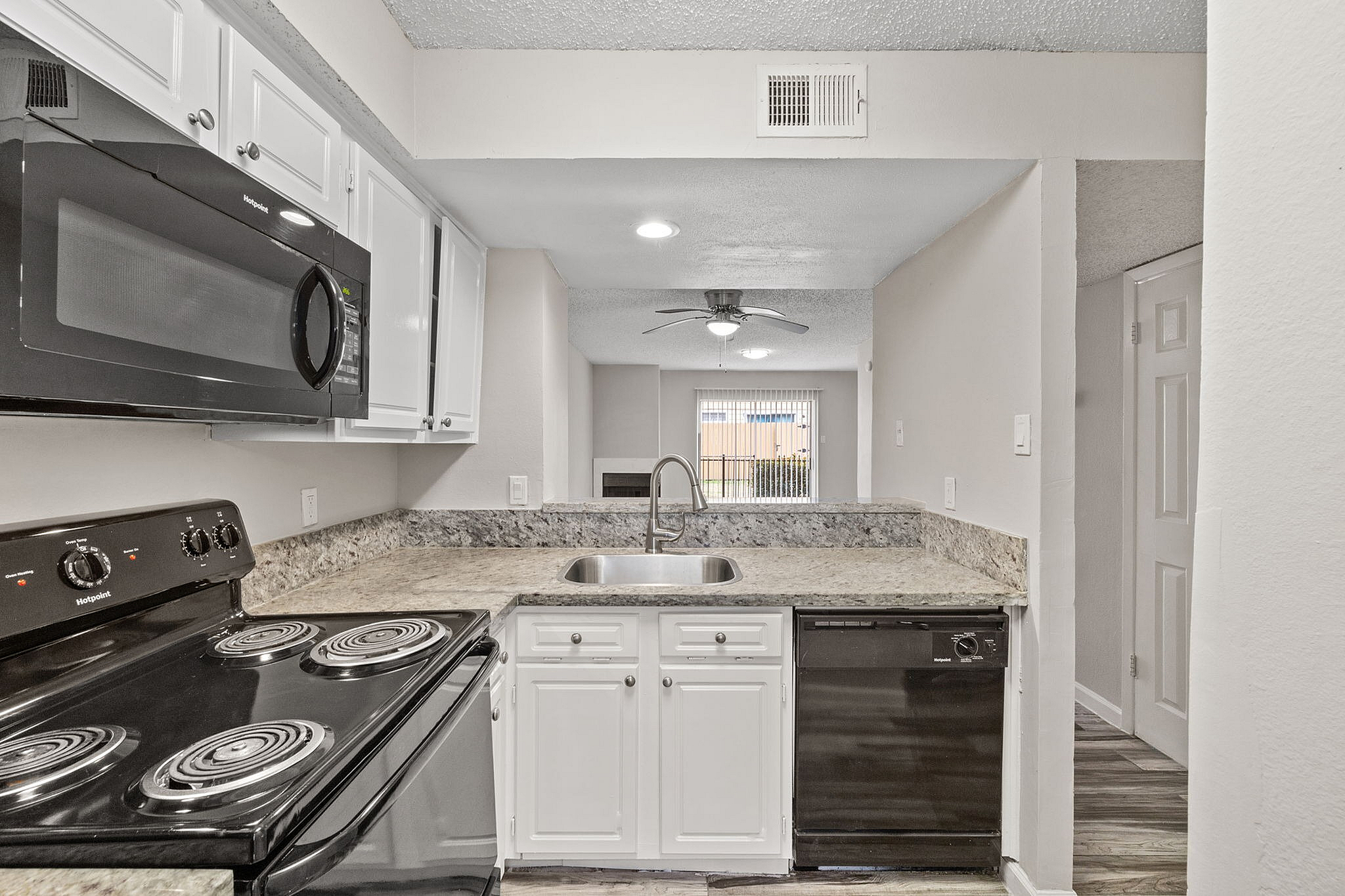 Modern kitchen with sleek granite countertops, black appliances, and open-plan design leading to a bright living area.
