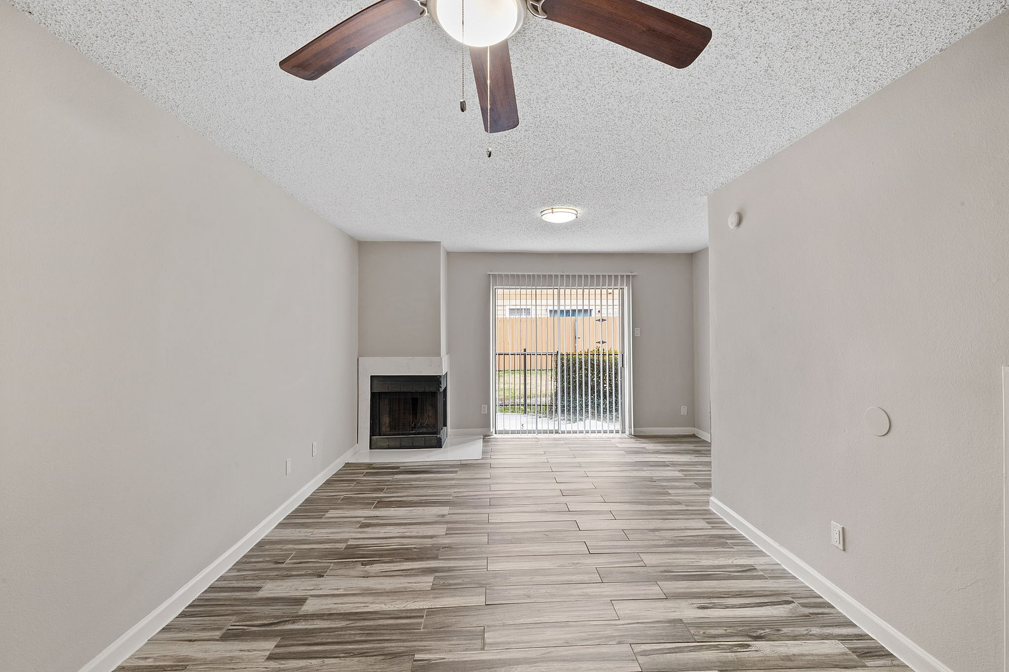 Bright living room with elegant wood-look tile flooring, cozy fireplace, and sliding doors leading to a private outdoor space.