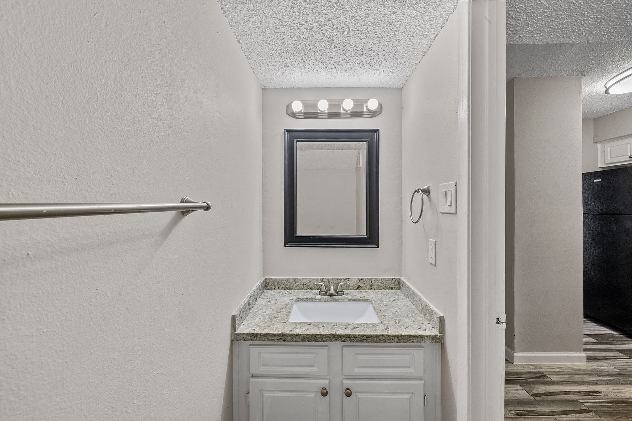 Bright bathroom with modern black framed mirror, elegant granite countertop, and stylish light fixtures.