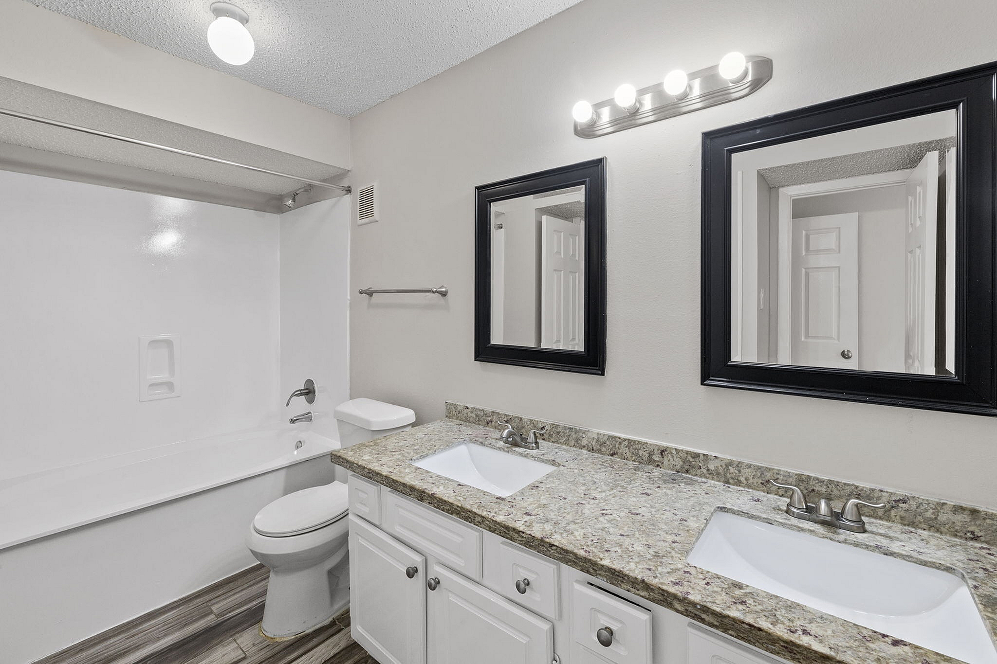 Elegant modern bathroom with dual sinks, granite countertop, and bright lighting.