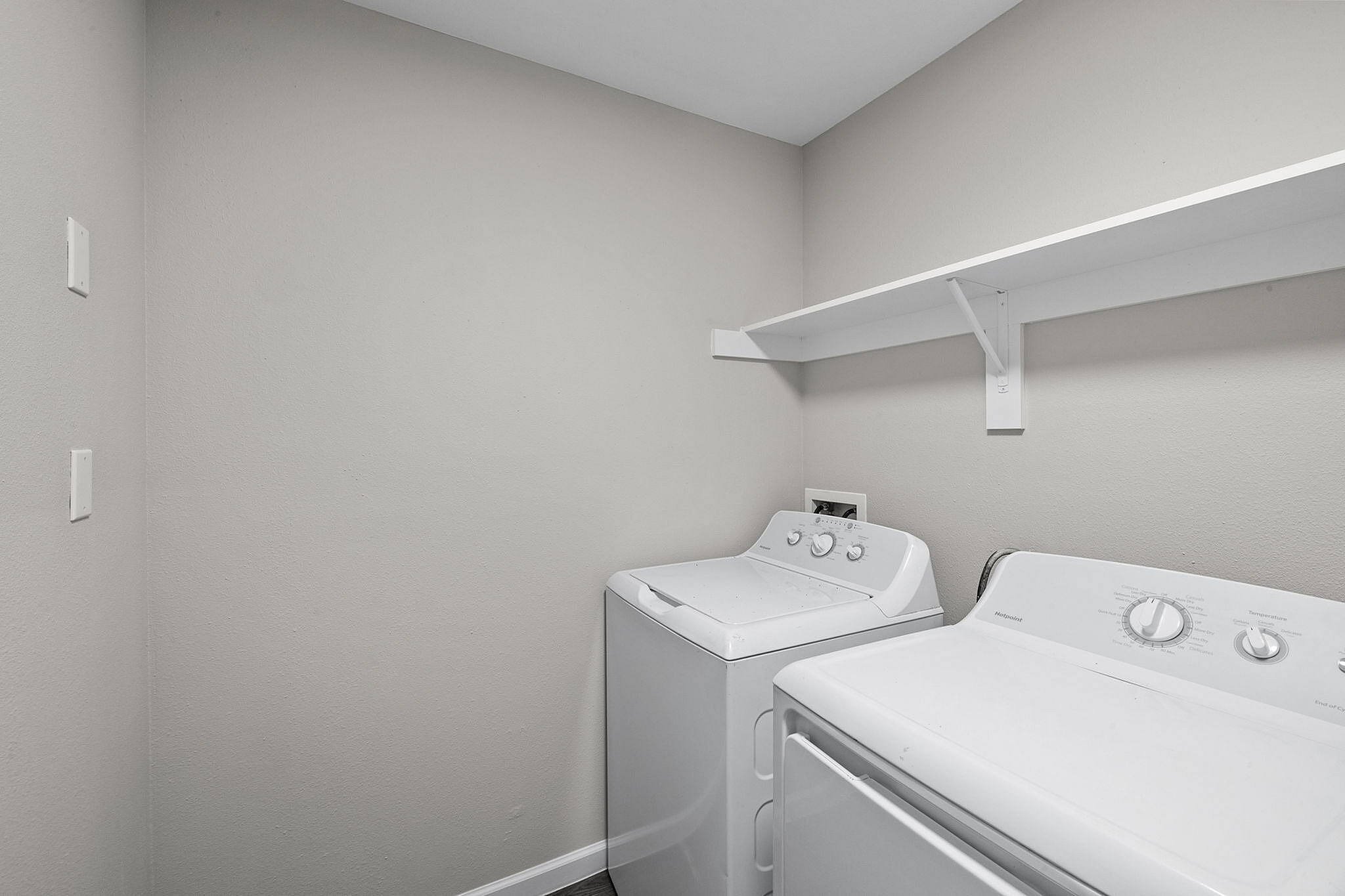 Modern laundry room with sleek washer and dryer, featuring a convenient wall-mounted shelf for storage.