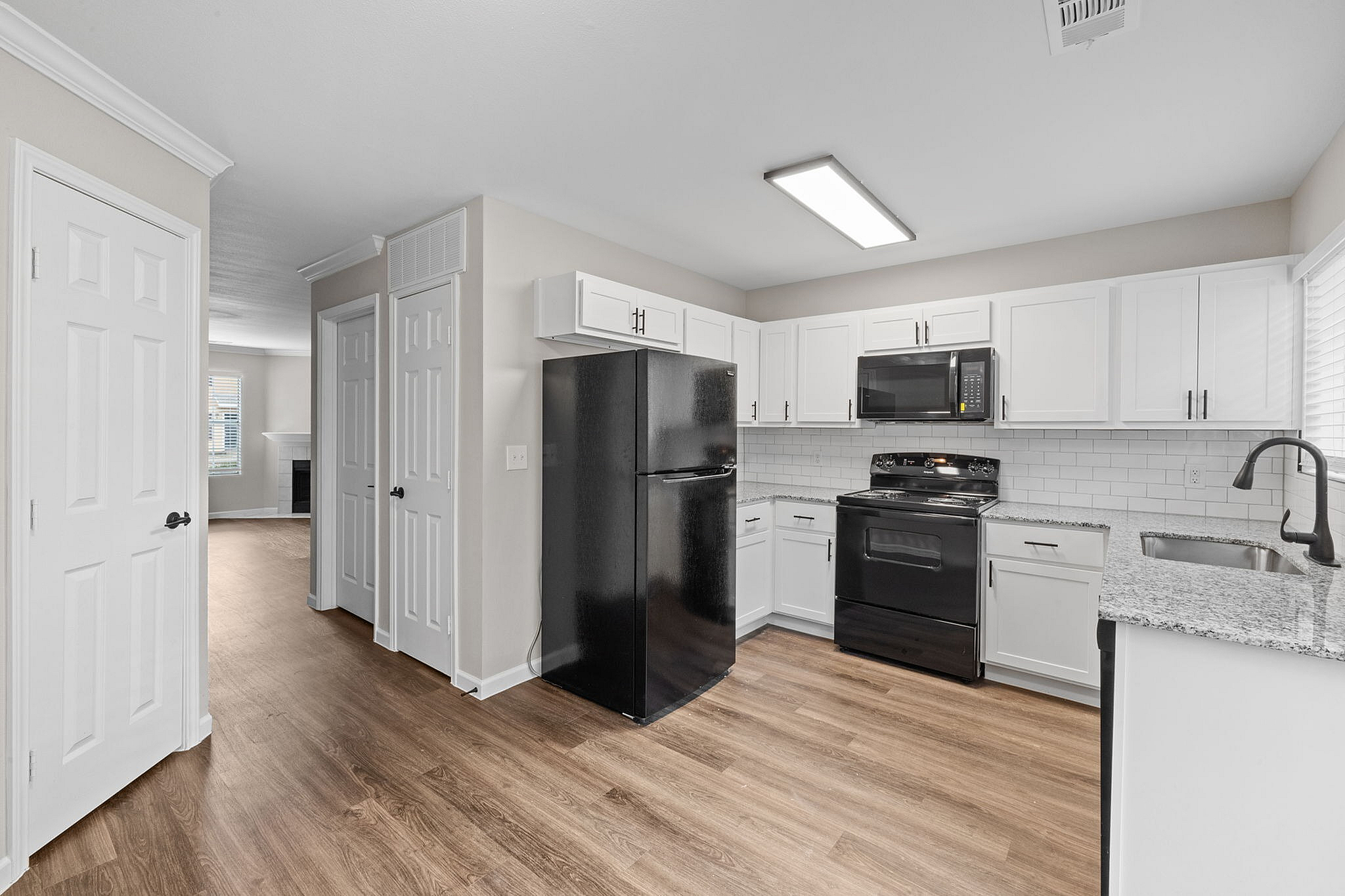 Bright and modern kitchen with sleek black appliances, white cabinetry, and hardwood floors opening into a cozy living area.