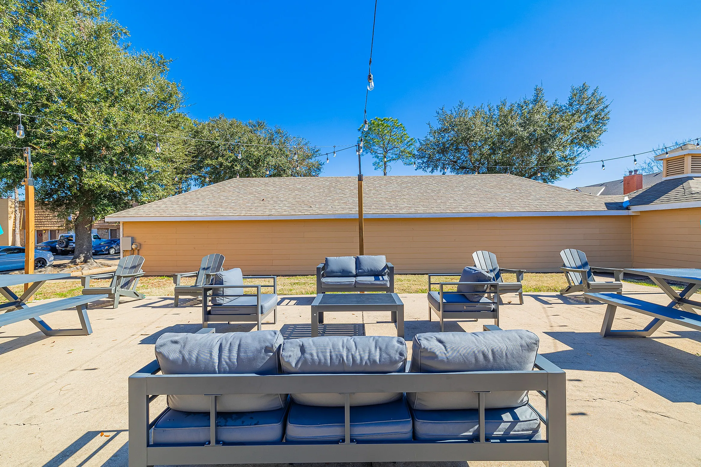 Inviting outdoor lounge area with modern seating and soft cushions, perfect for gatherings, set against a sunny backdrop under string lights.