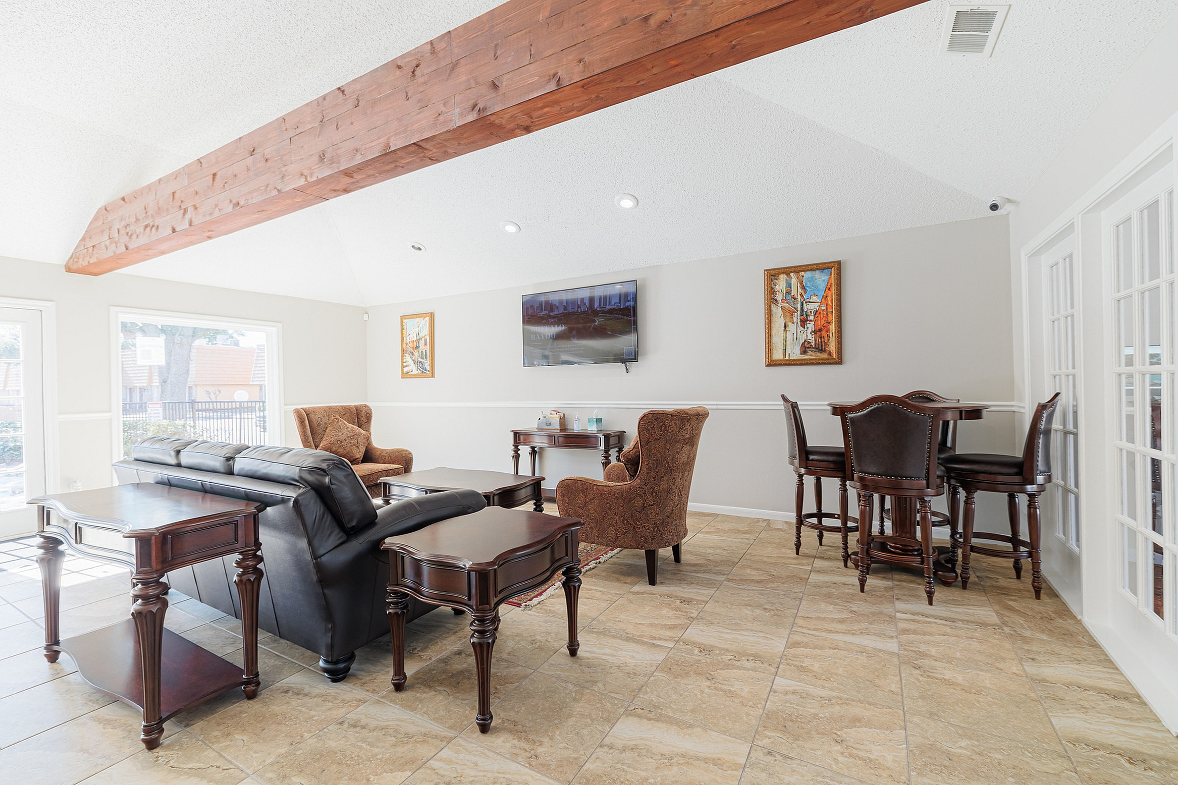 Elegant living room with vaulted ceiling and wooden beam, featuring plush seating, sleek leather sofas, and sophisticated dark wood furniture, bathed in natural light from large windows.