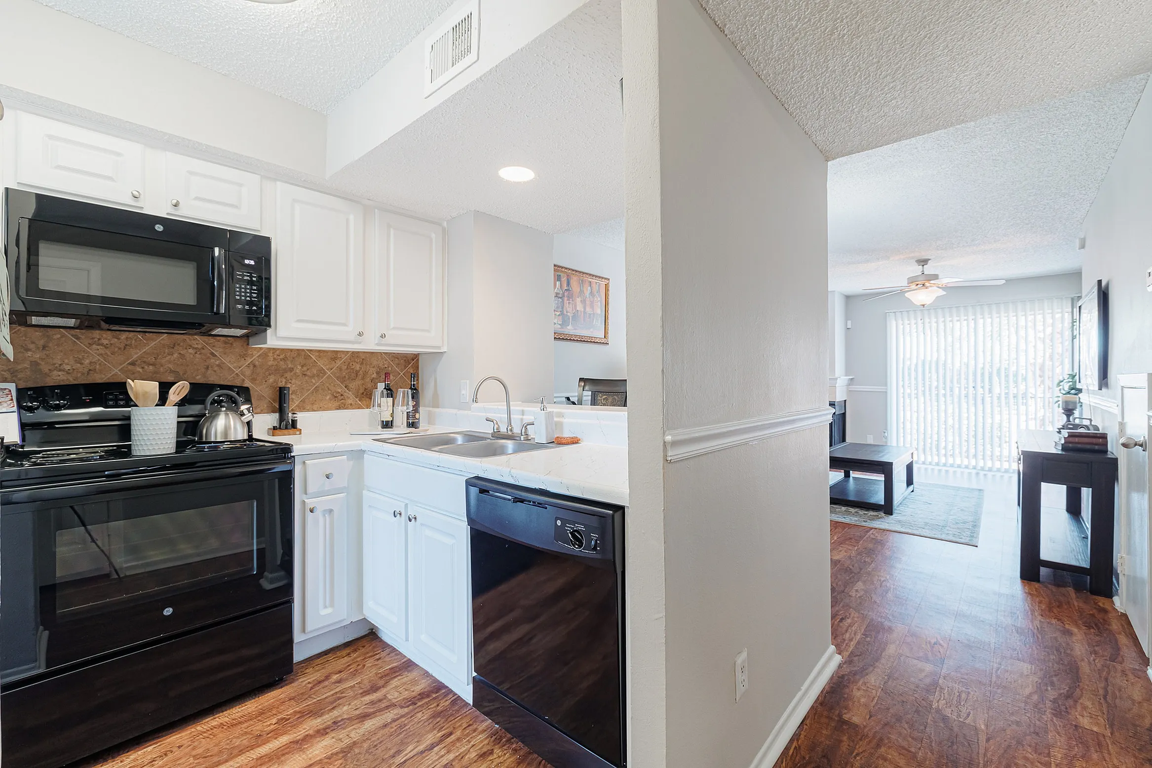 Bright and inviting kitchen with modern black appliances, wooden floors, and open view to a sunlit living room.
