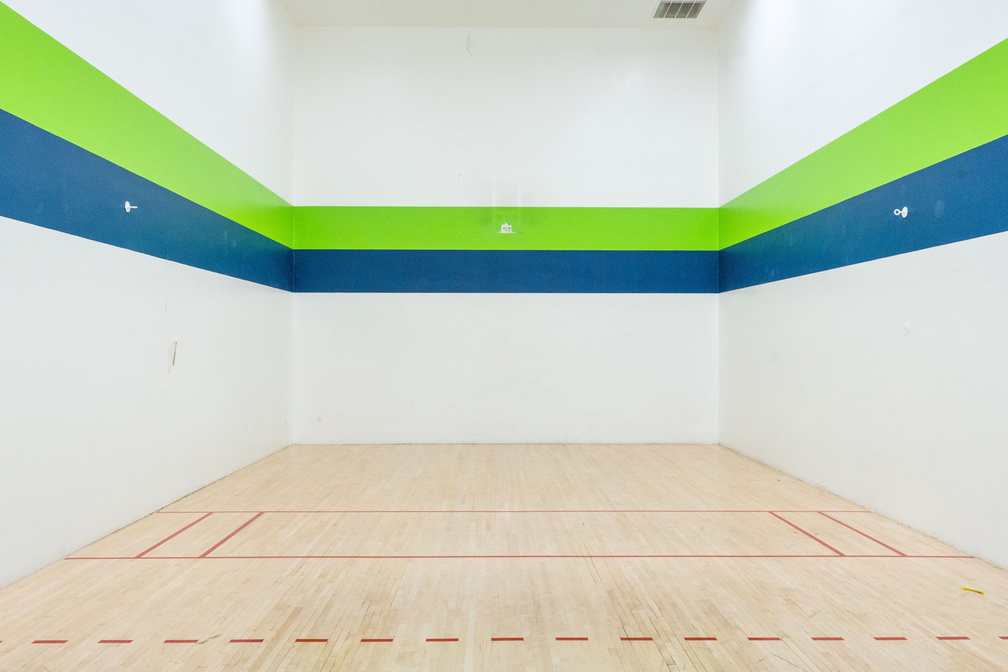 Bright squash court with modern colorful stripe design featuring a polished wooden floor and ample space for playing.