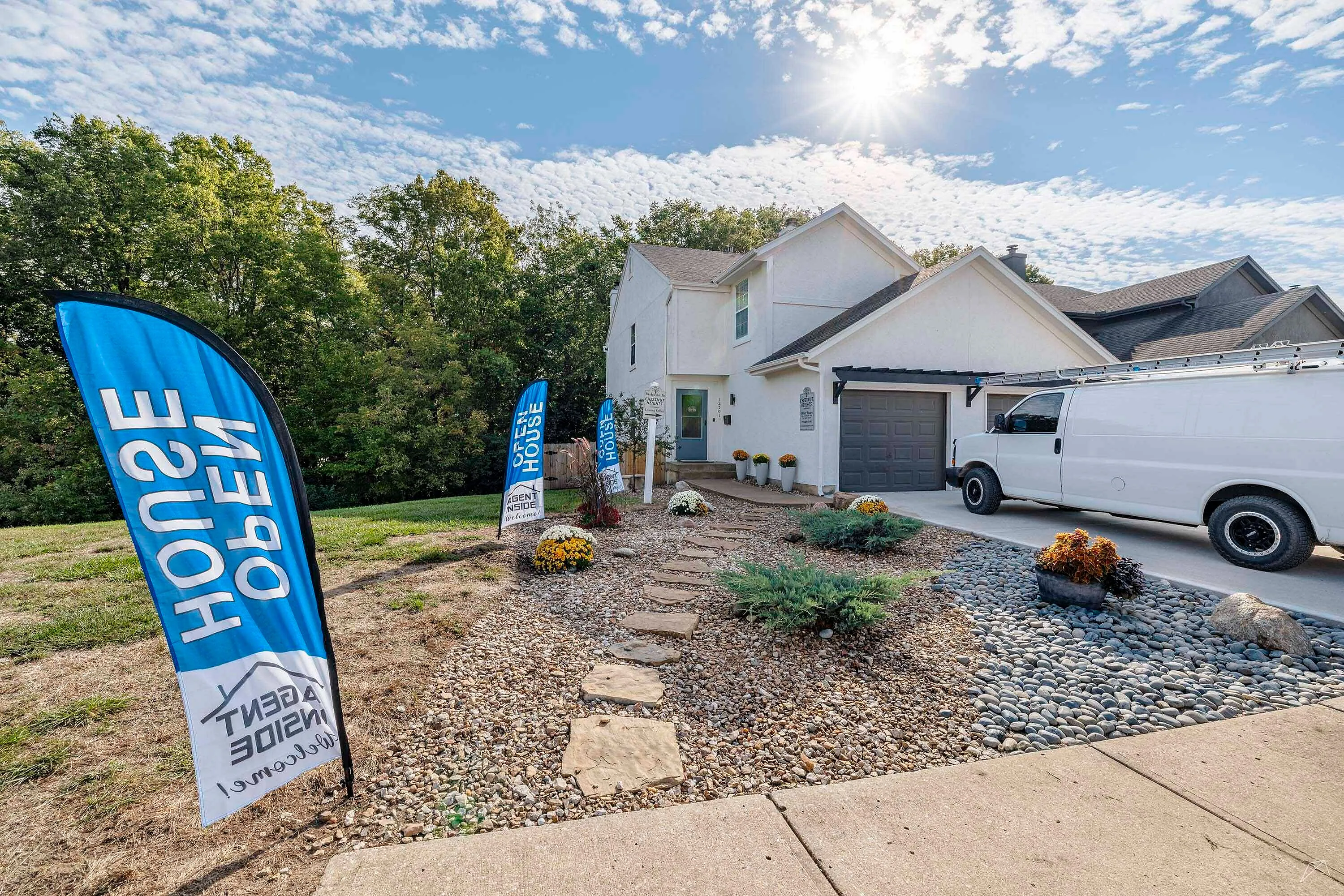 Charming two-story home with a beautifully landscaped front yard, open house signs, and a sunlit driveway, perfect for modern living.