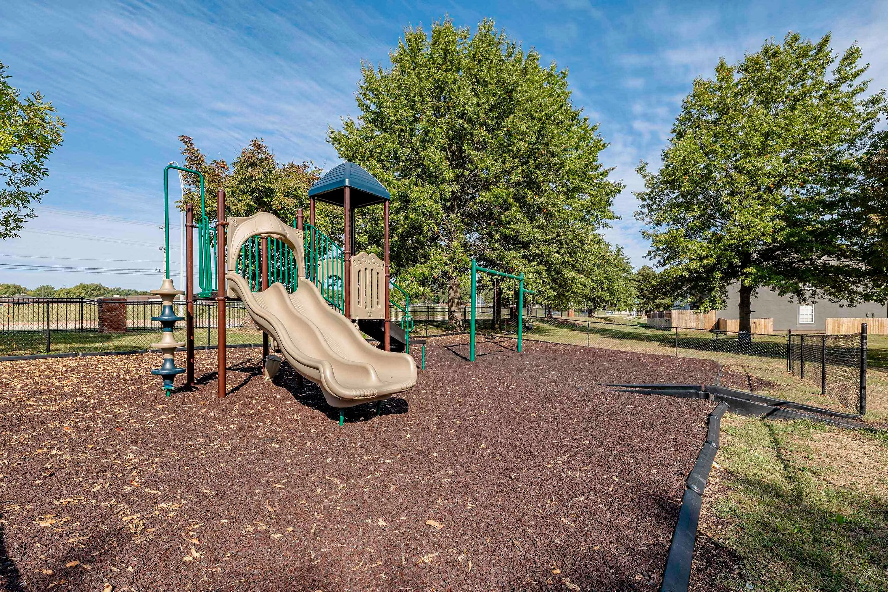 Inviting apartment community playground with a modern slide set amidst lush trees, perfect for family fun.