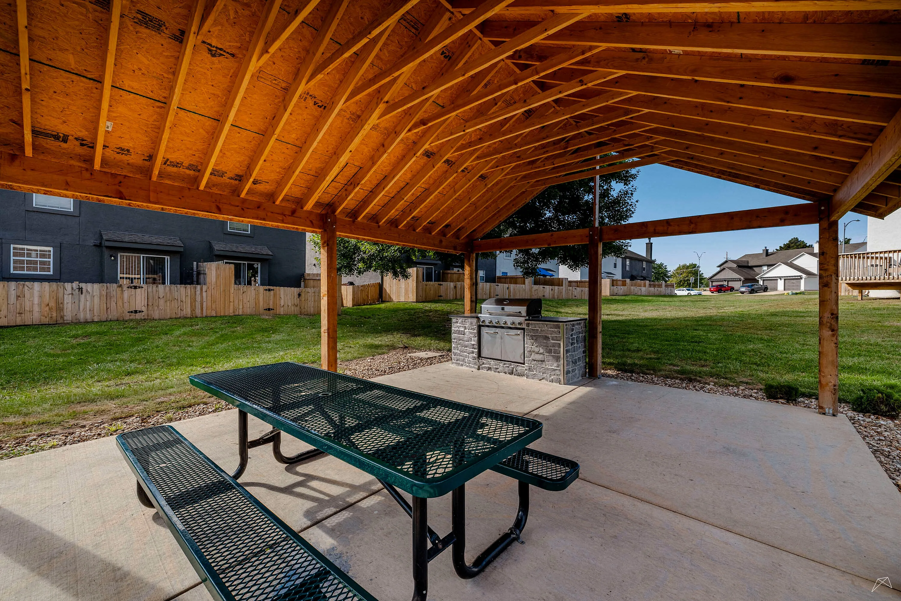Inviting outdoor pavilion with a rustic wooden ceiling, picnic table, and built-in grill, perfect for gatherings and outdoor enjoyment.