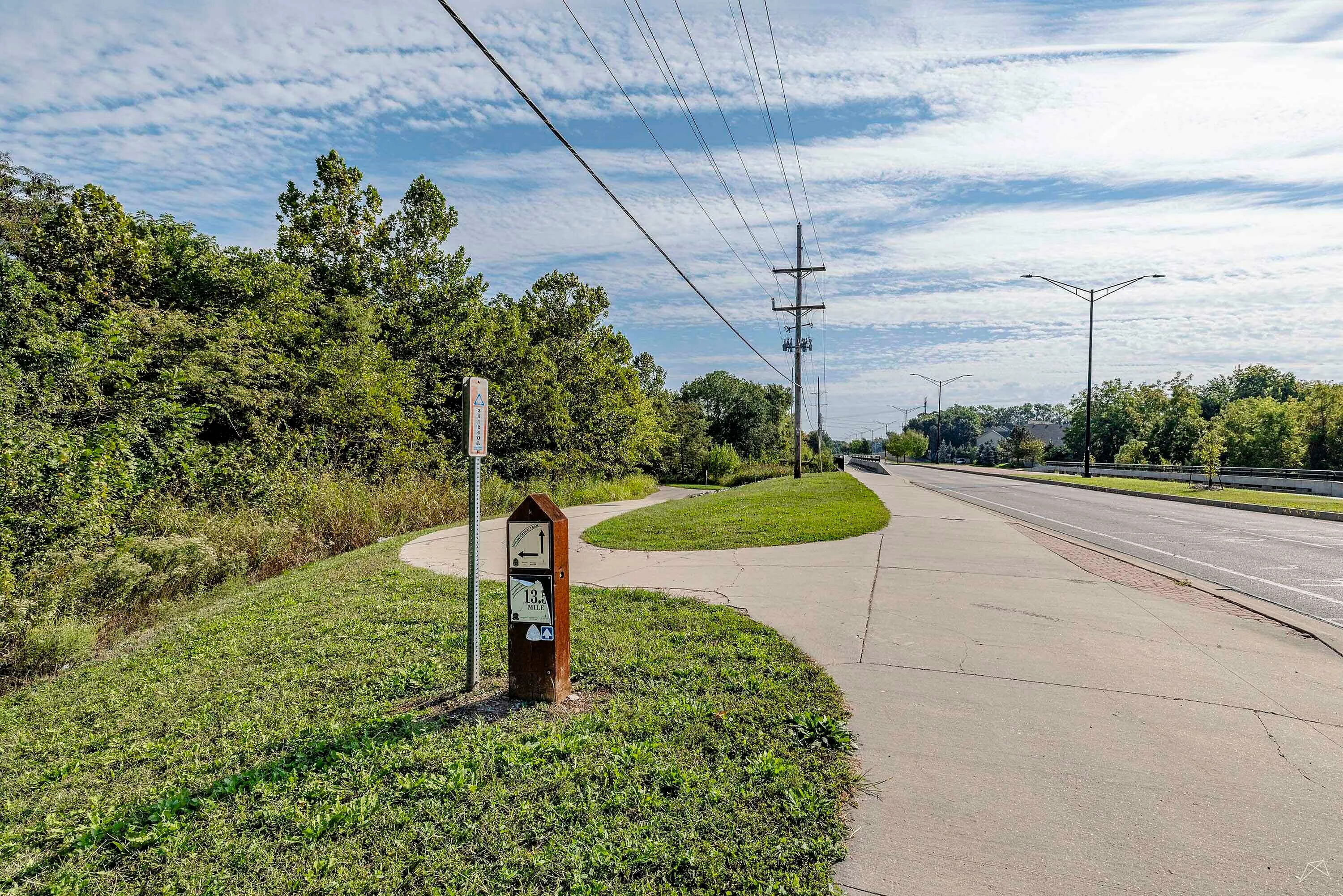 Scenic sidewalk view with lush greenery and clear skies, showcasing a peaceful suburban pathway ideal for walking and biking.