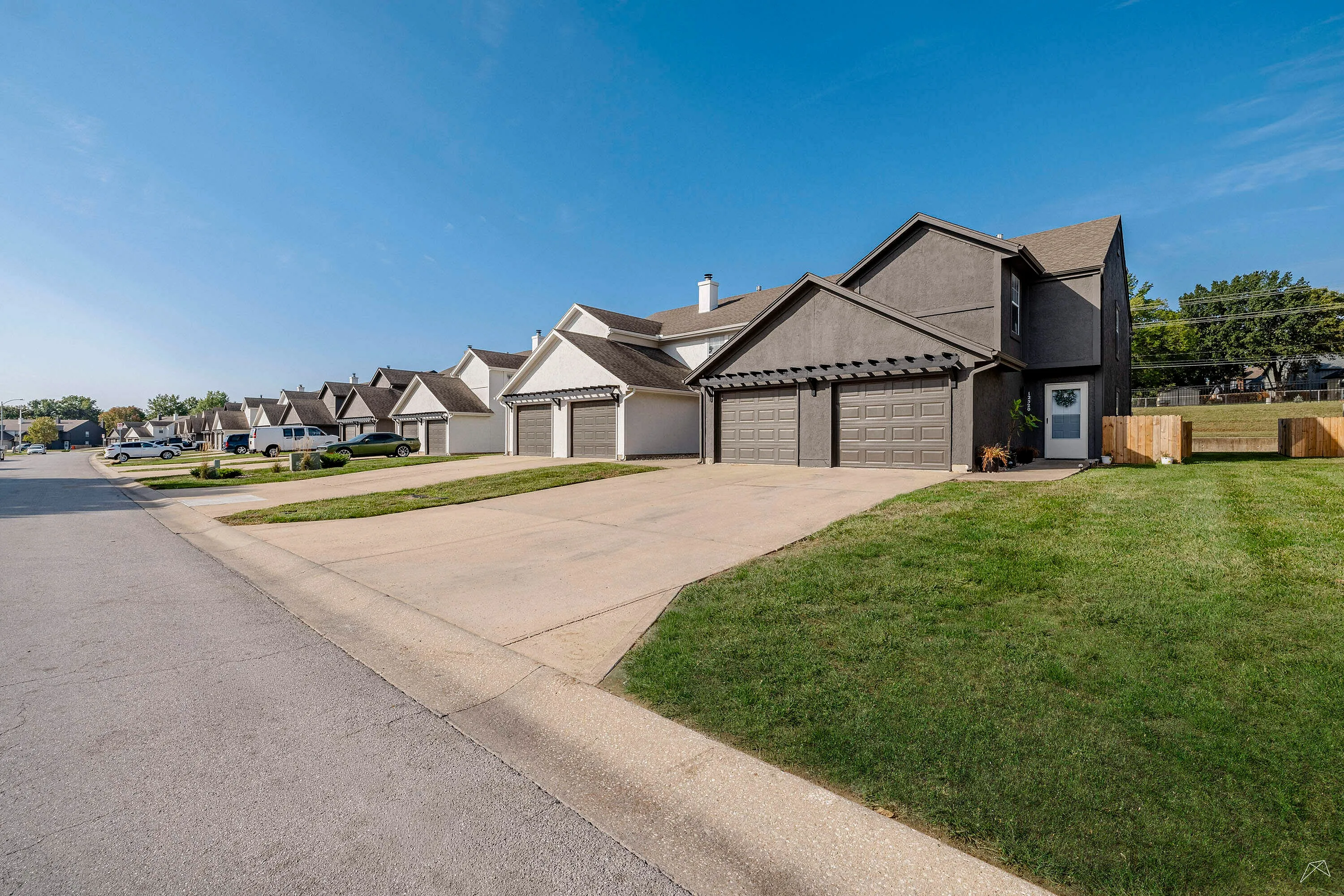 Charming suburban street lined with modern townhouses, each featuring double garages and neatly manicured lawns under a clear blue sky.