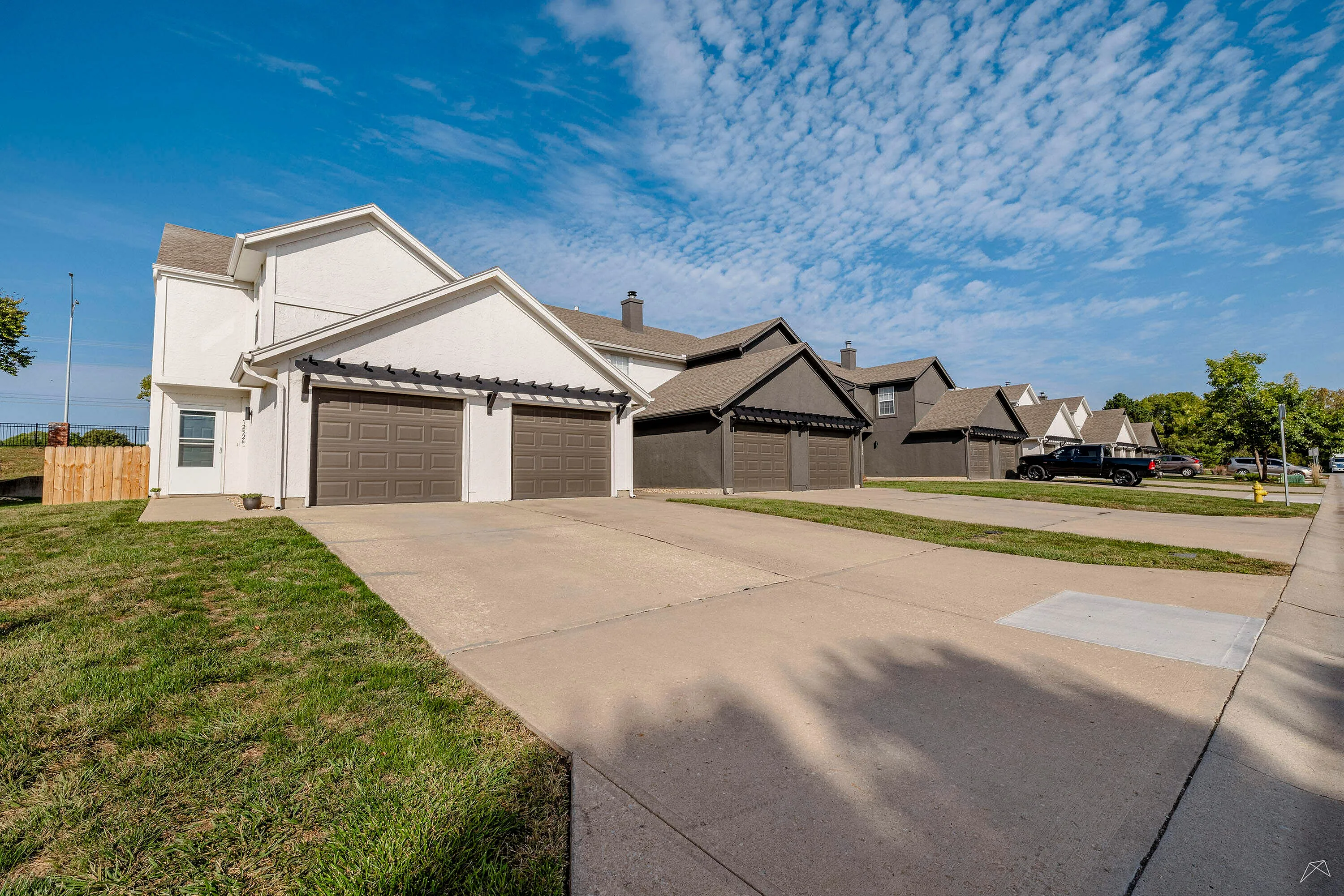 Charming suburban street lined with modern duplexes featuring clean driveways and well-maintained lawns under a vibrant blue sky.