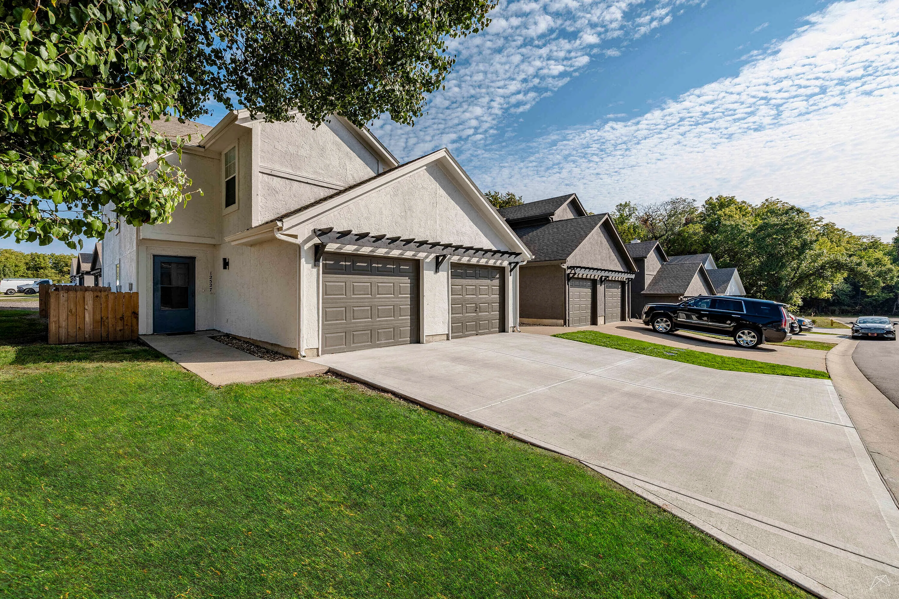 Charming suburban duplex with modern garages, set in a lush, green neighborhood under a bright, blue sky.