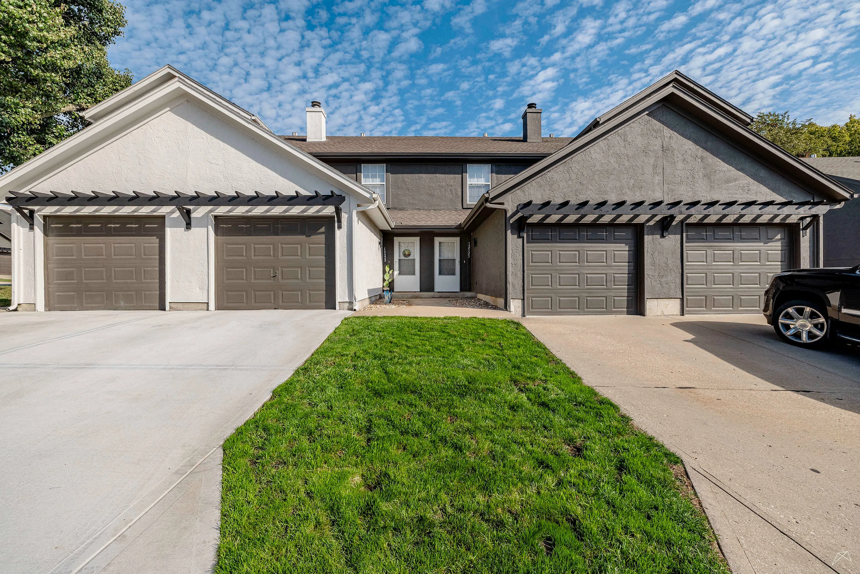 Charming duplex with three garages and manicured lawn under a bright blue sky, showcasing curb appeal and functionality.