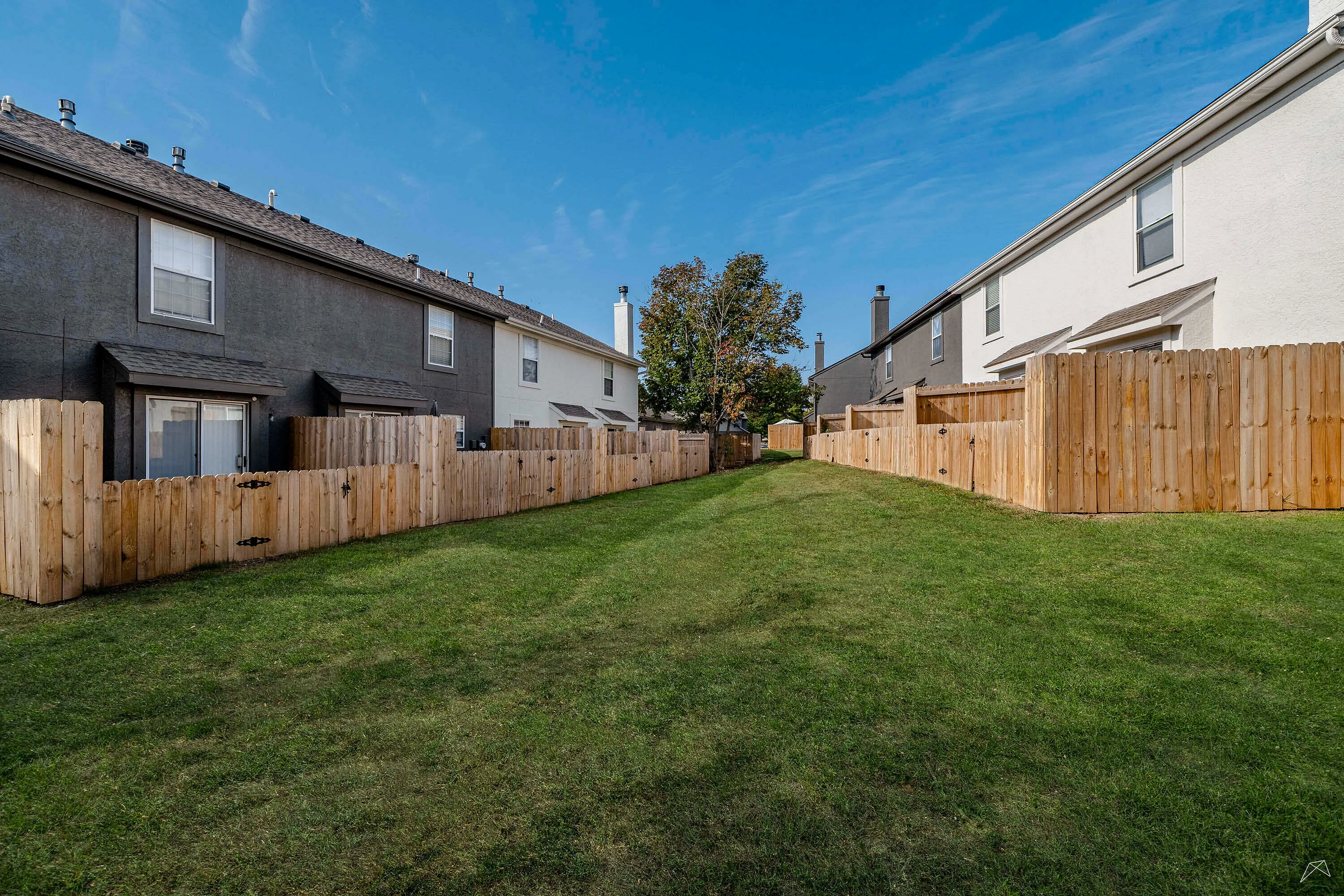 Charming townhouse backyard with lush green grass and private wooden fences under a clear blue sky.