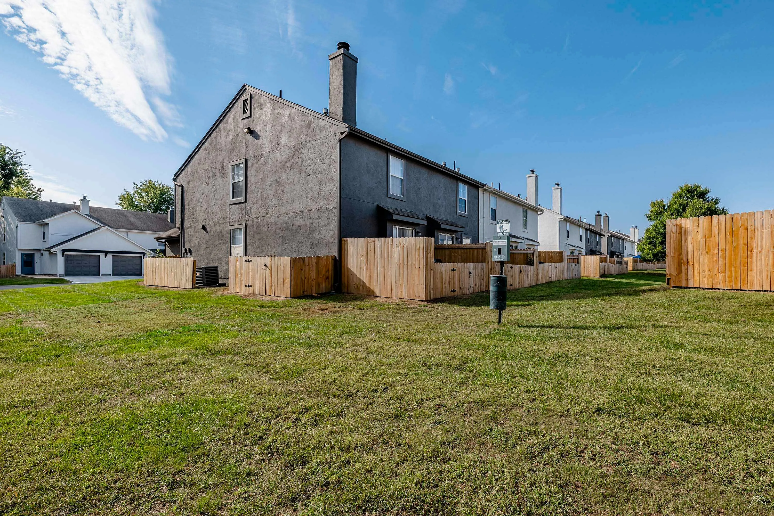 Charming row of townhouses with private fenced yards, set against a clear blue sky and lush green lawn.