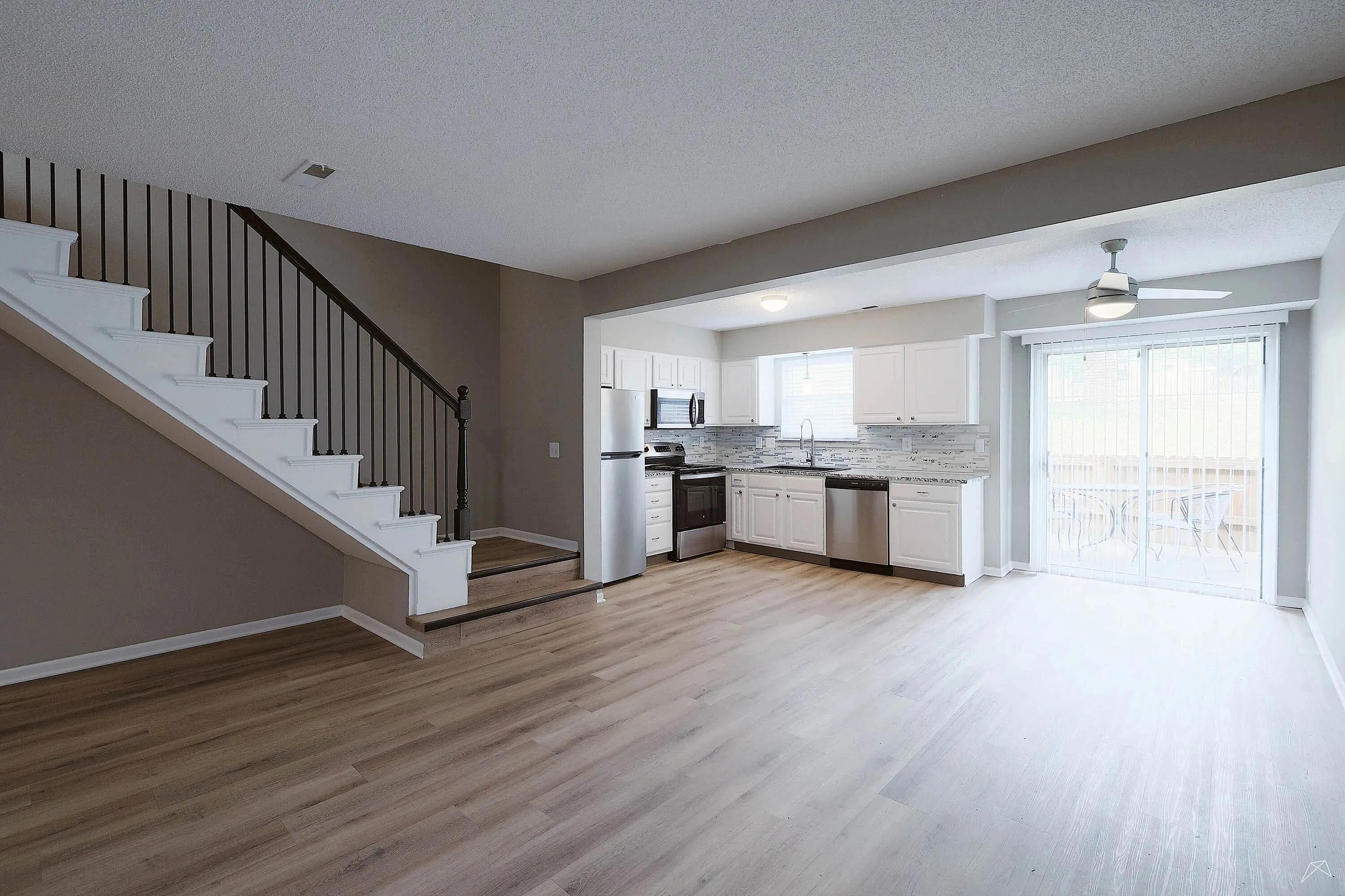 Modern open-concept kitchen with sleek white cabinetry, stainless steel appliances, and bright sliding glass doors leading to a scenic outdoor space.